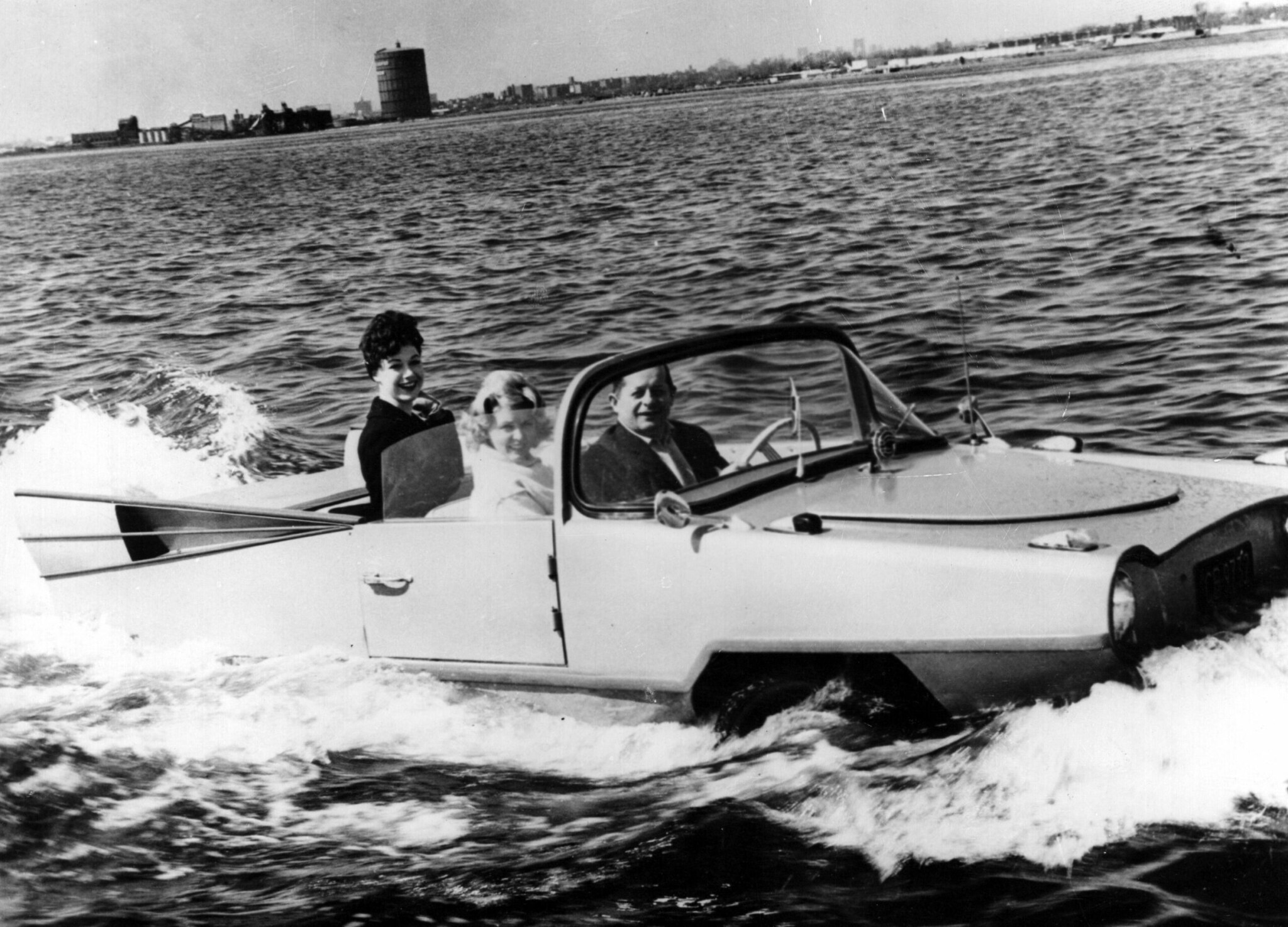 Ein Schwarz-Weiß-Foto eines Amphibienautos mit drei Personen an Bord Ein Schwarz-Weiß-Foto eines Amphibienautos mit drei Personen an Bord