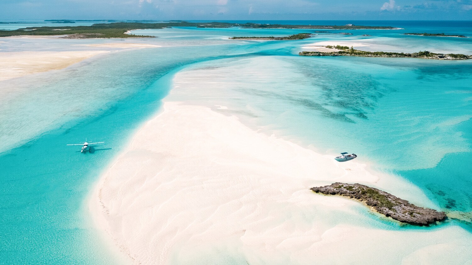 Heller Strand und türkisblaues Meer, auf dem ein Wasserflugzeug landet.