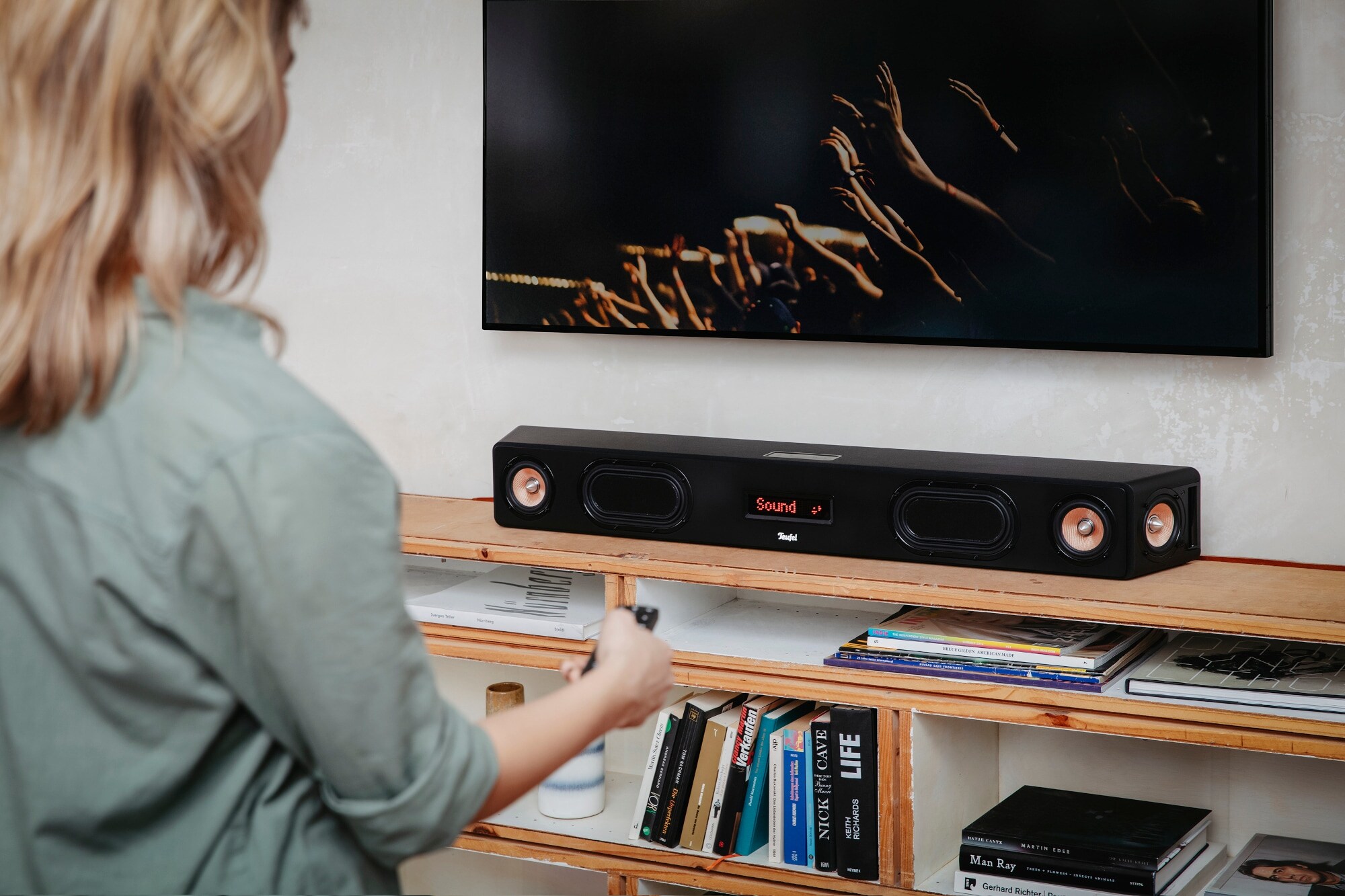 Eine Frau bedient mit einer Fernbedienung eine Soundbar unterhalb eines TV-Gerätes