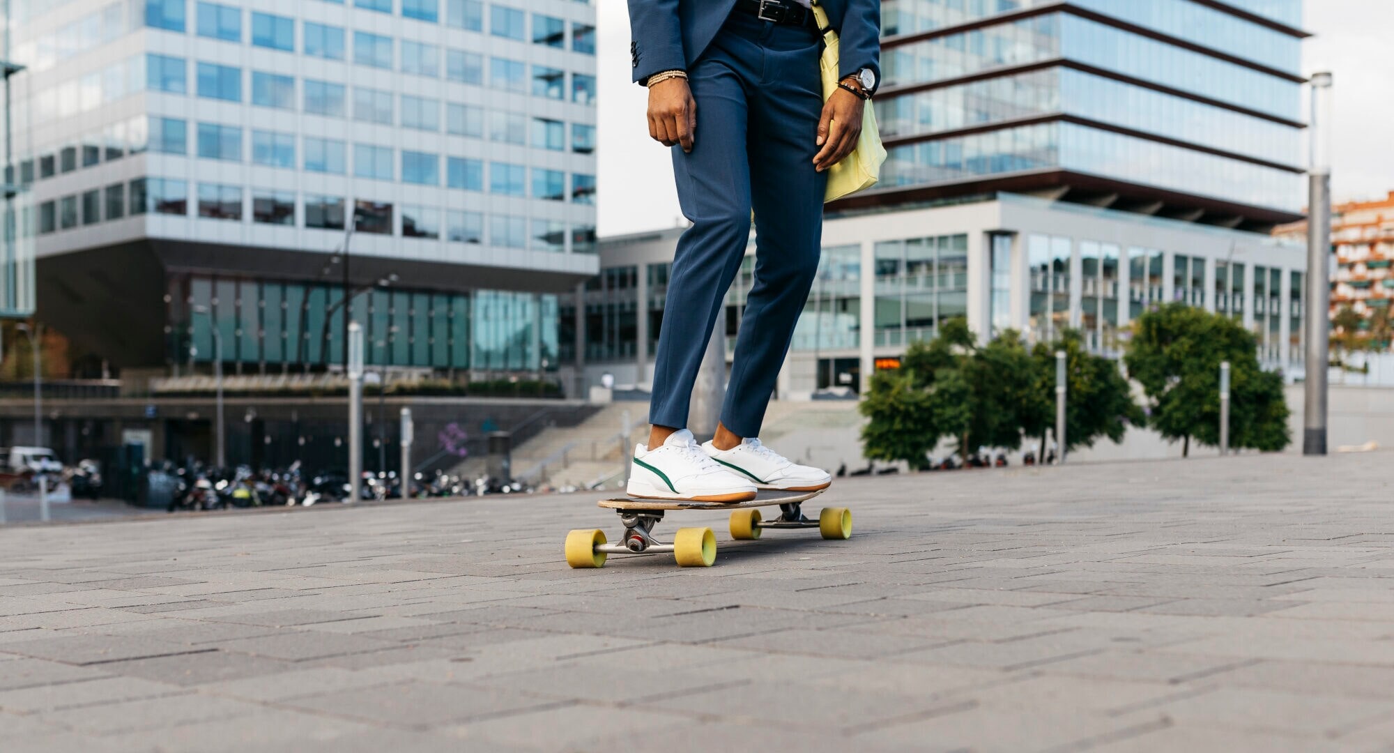 Zwei Beine auf einem Skateboard, die Person trägt eine Anzughose und weiße Sneaker