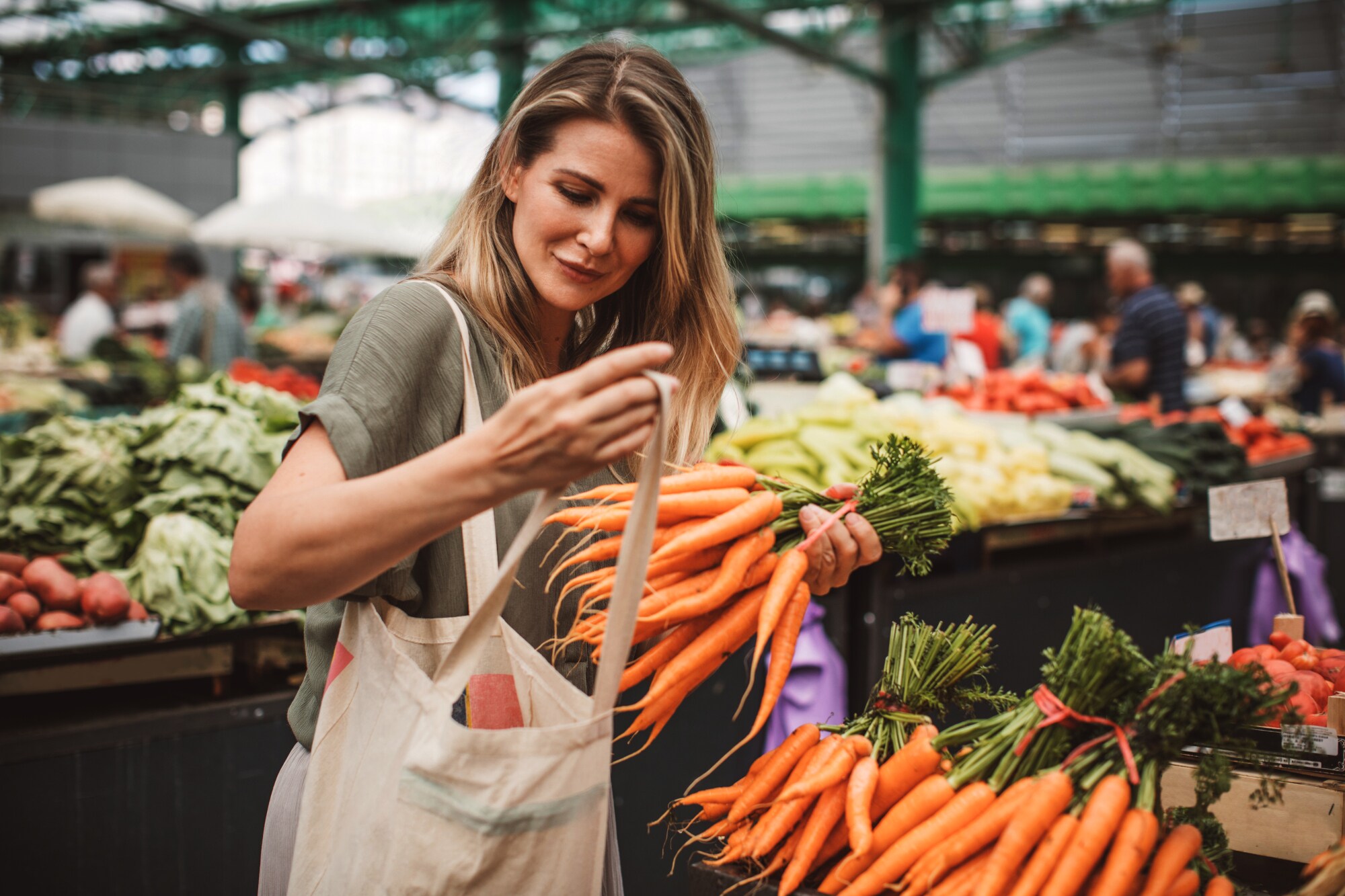 Eine junge Frau auf einem Wochenmarkt steckt ein Bund Möhren in ihren Jutebeutel