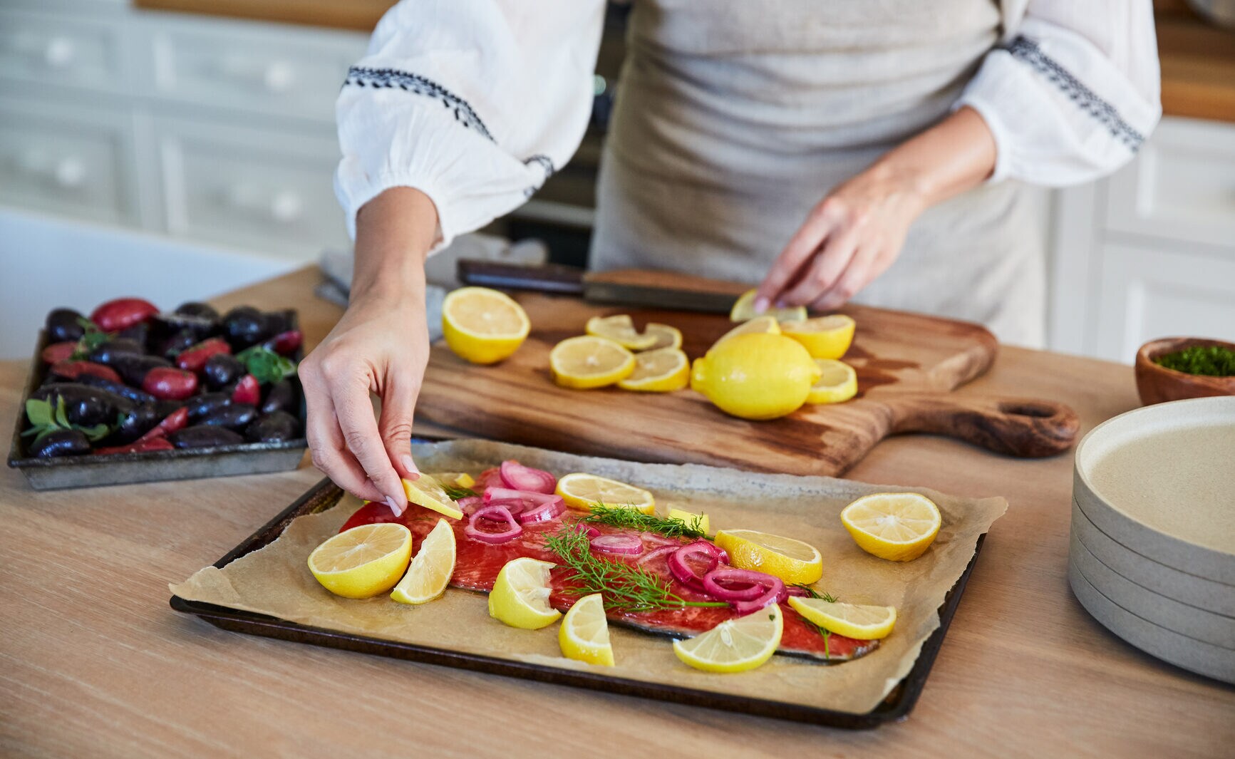 Eine Frau bereitet Lachs mit Zitronenscheiben auf einem Blech in einer Küche zu Eine Frau bereitet Lachs mit Zitronenscheiben auf einem Blech in einer Küche zu