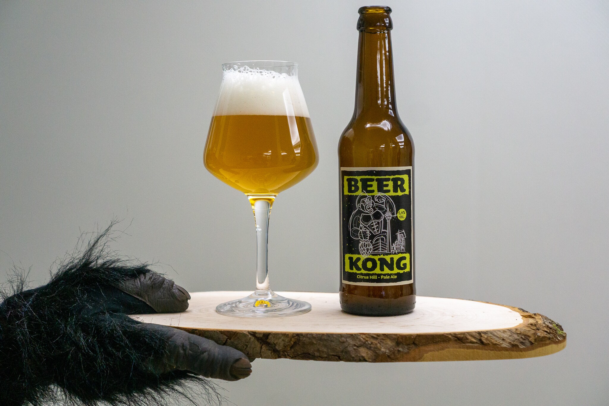 Ein Glas Bier und eine Flasche auf einer Holzplatte, die von einer Hand in einem Affenkostüm gehalten wird