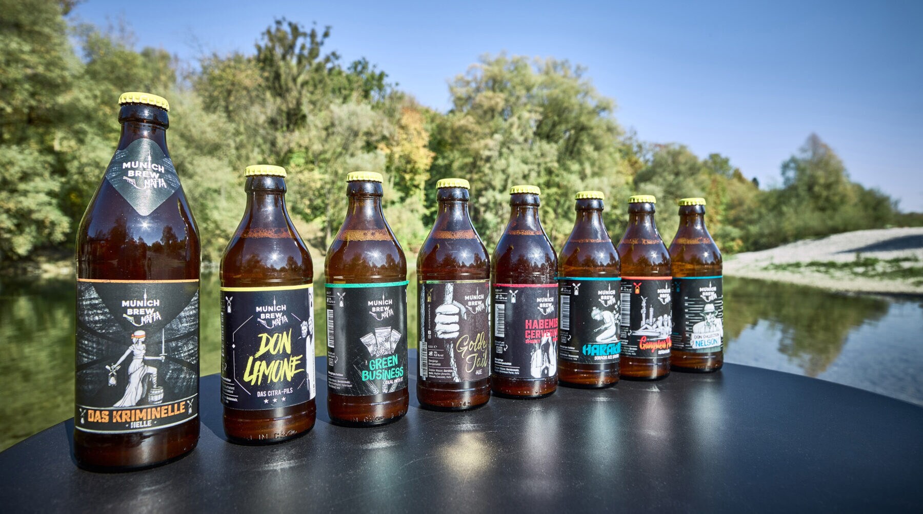 Eine Reihe Bierflaschen mit modern designten Labels auf einem Tisch an einem See Eine Reihe Bierflaschen mit modern designten Labels auf einem Tisch an einem See