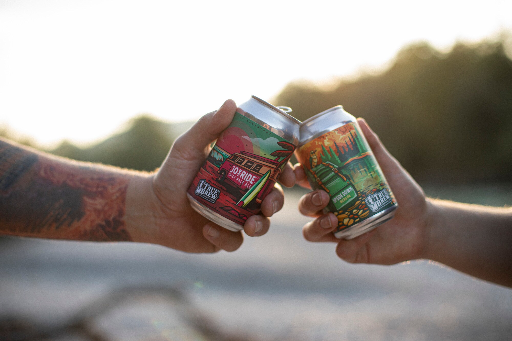 Zwei Hände, die mit bunt designten Bierdosen anstoßen Zwei Hände, die mit bunt designten Bierdosen anstoßen