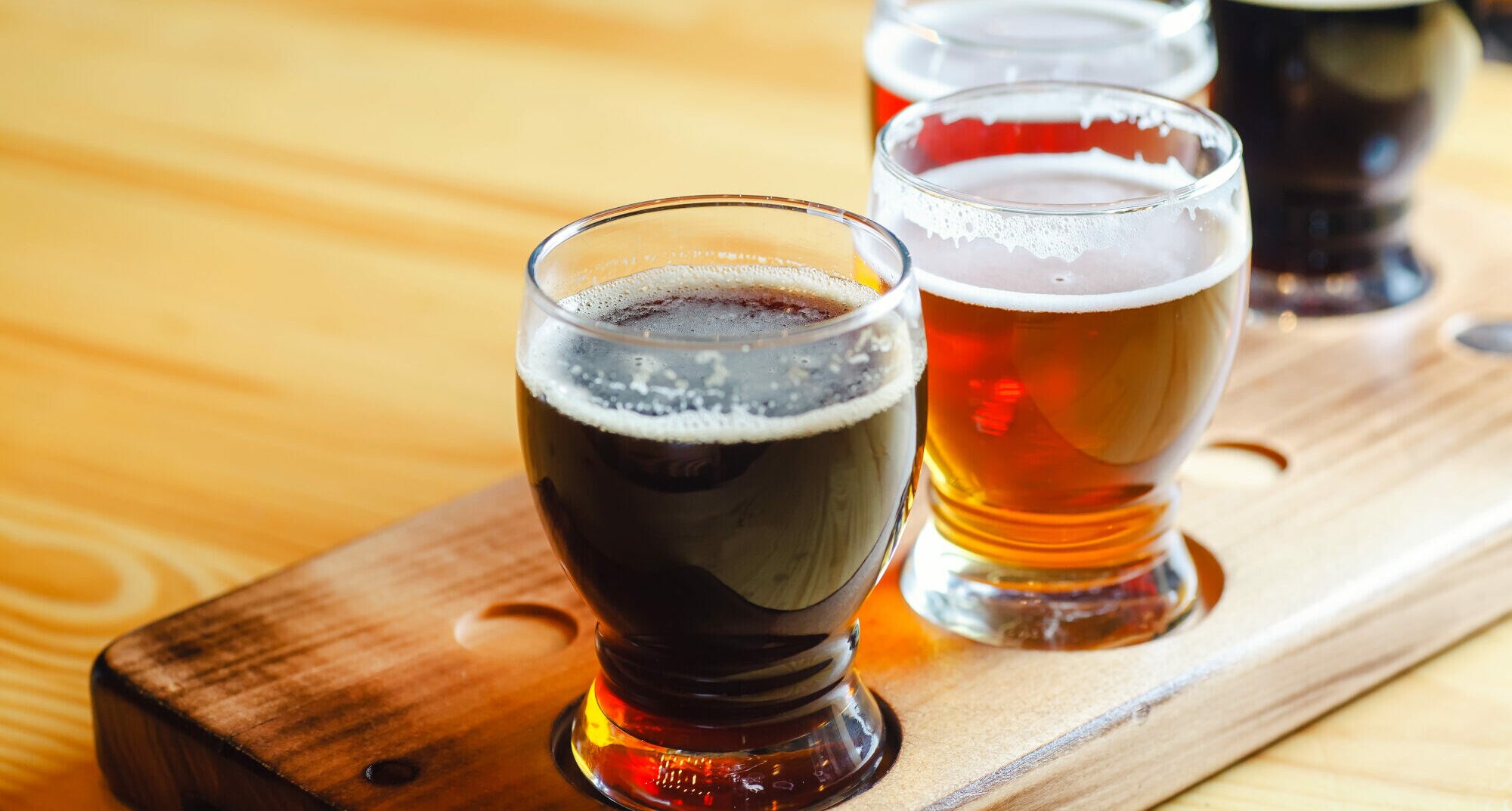 Vier mit unterschiedlich farbigem Bier gefüllte Gläser auf einem Tasting-Brett