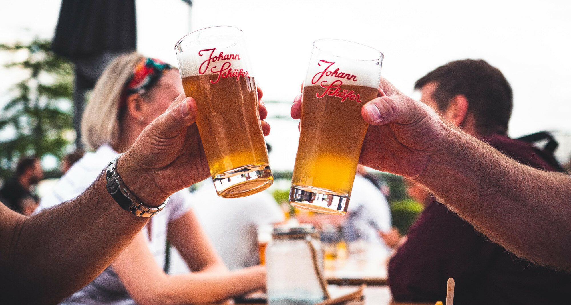 Zwei Menschen prosten sich mit einem gezapften Bier im Glas zu Zwei Menschen prosten sich mit einem gezapften Bier im Glas zu