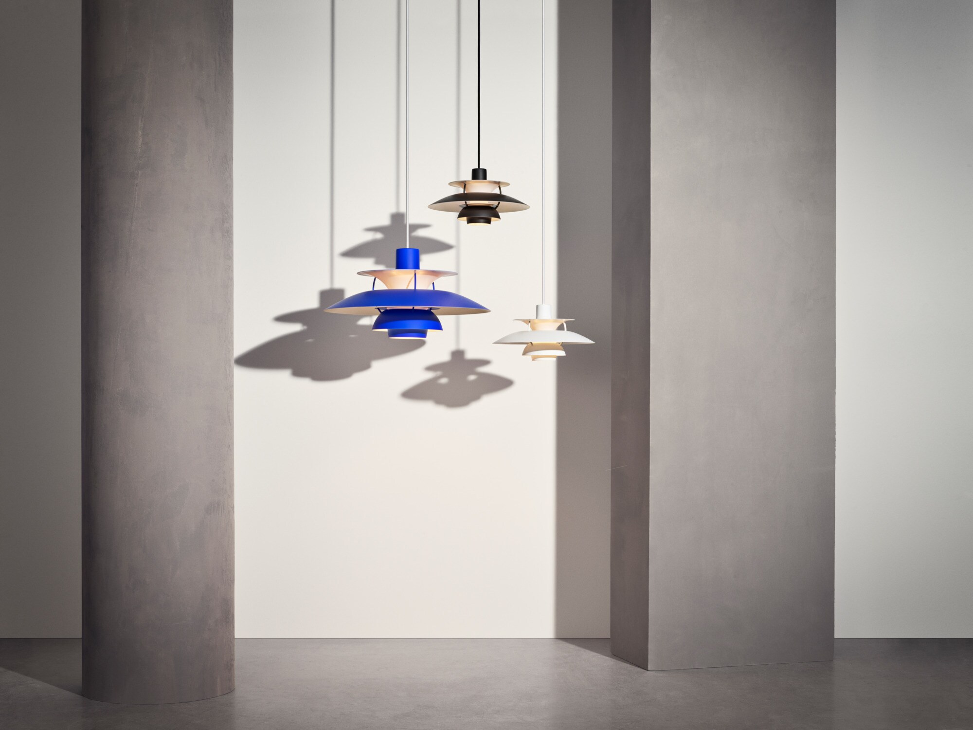 Drei Pendelleuchten PH 5 hängen von der Decke in einem kargen Raum.