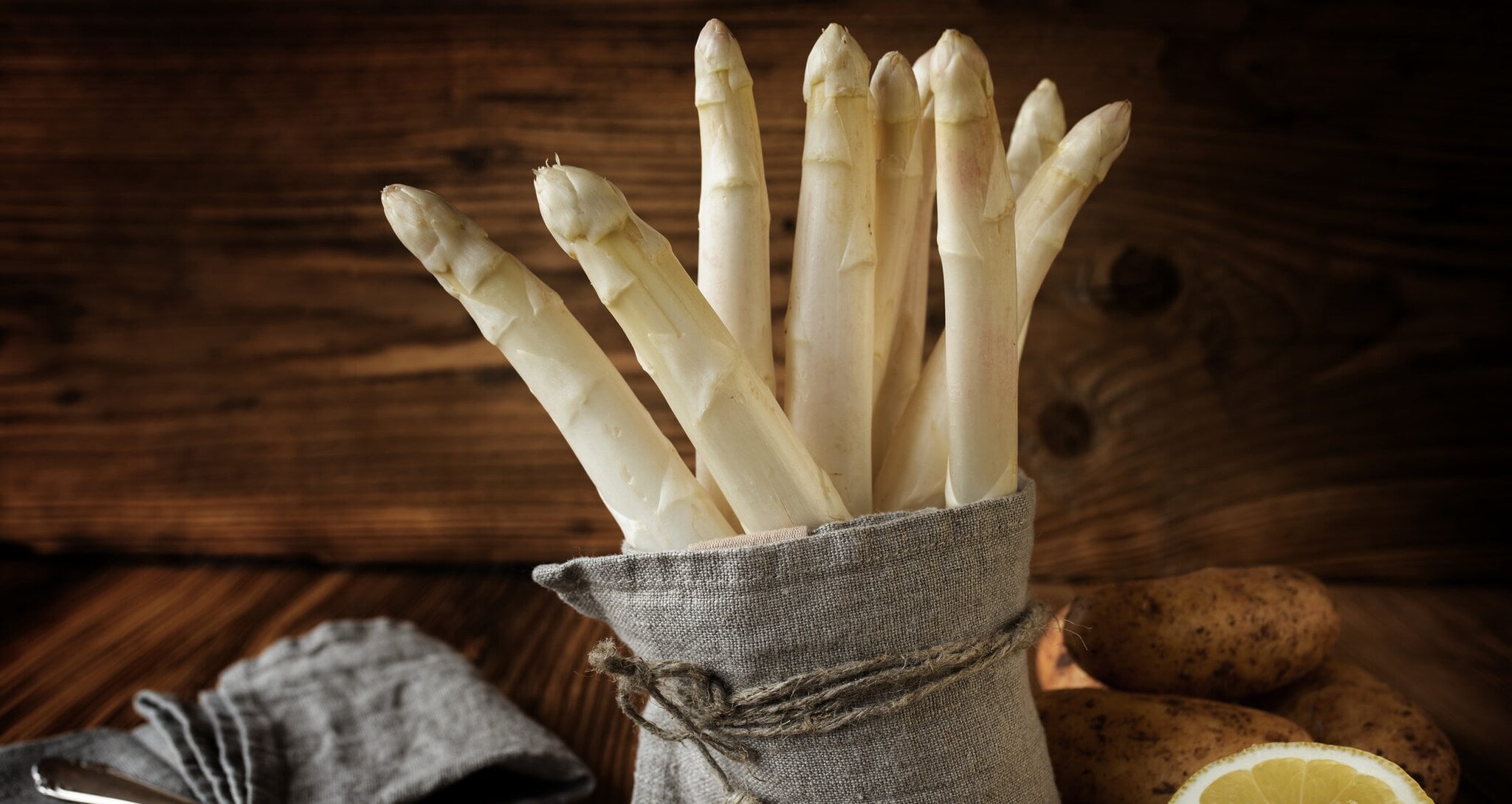 Ein Bund Spargel ist in einem Leinentuch eingeschlagen und steht auf einem rustikalem Holzbrett Ein Bund Spargel ist in einem Leinentuch eingeschlagen und steht auf einem rustikalem Holzbrett