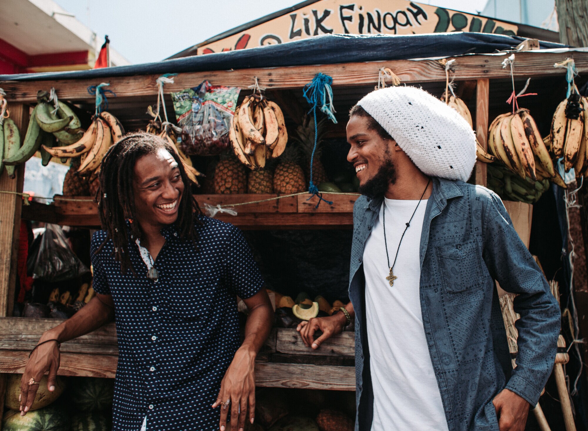 Zwei Männer mit Dreadlocks stehen vor einem Straßenstand mit Obst Zwei Männer mit Dreadlocks stehen vor einem Straßenstand mit Obst