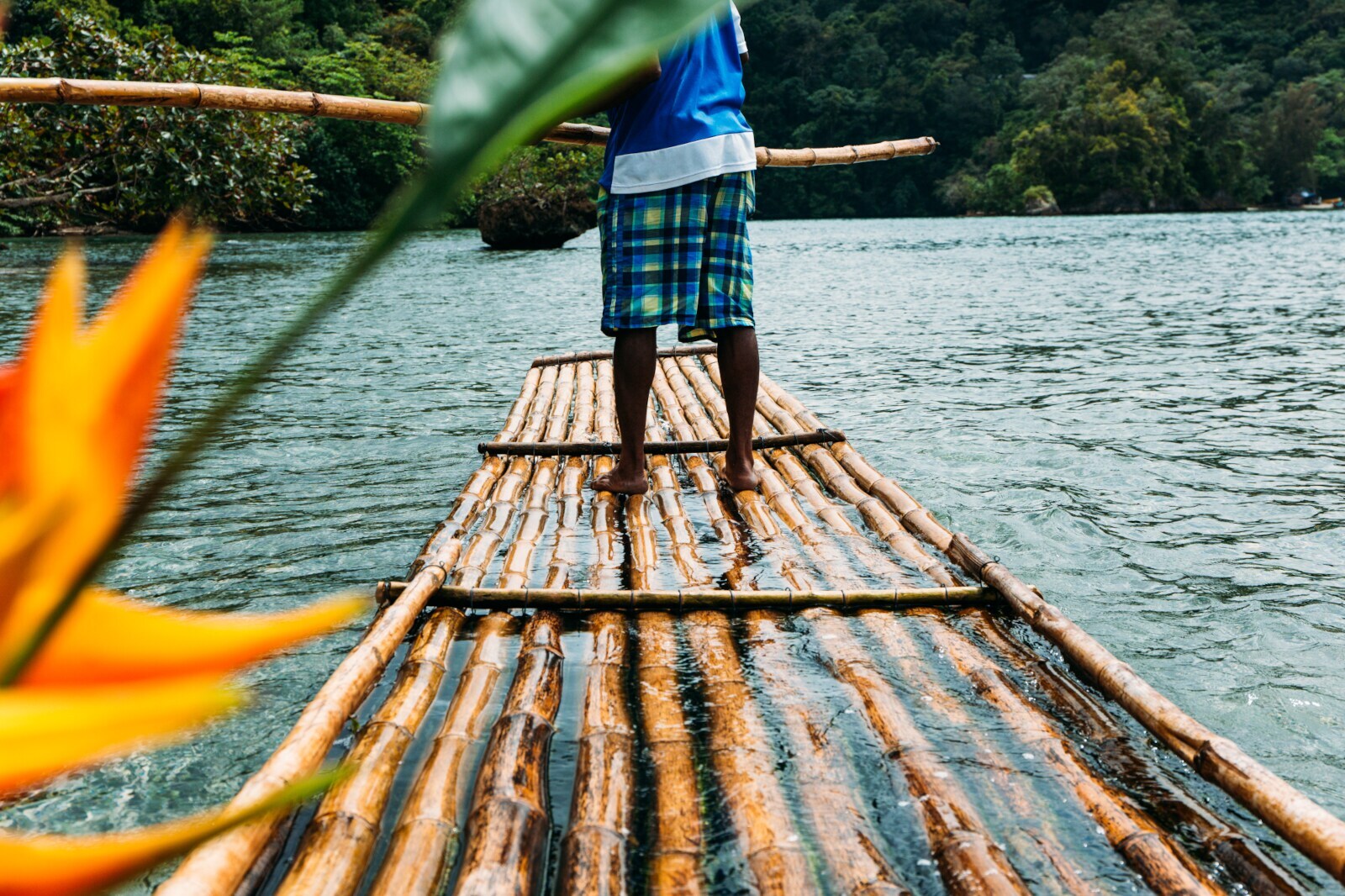 Ein Mann steuert auf einem Bambusfloß über einen Fluss