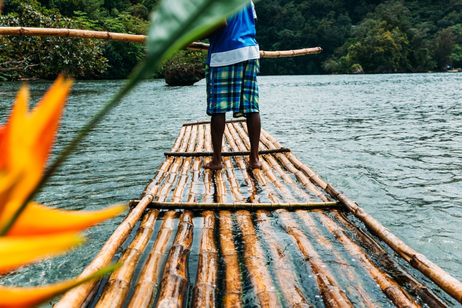Ein Mann steuert auf einem Bambusfloß über einen Fluss Ein Mann steuert auf einem Bambusfloß über einen Fluss