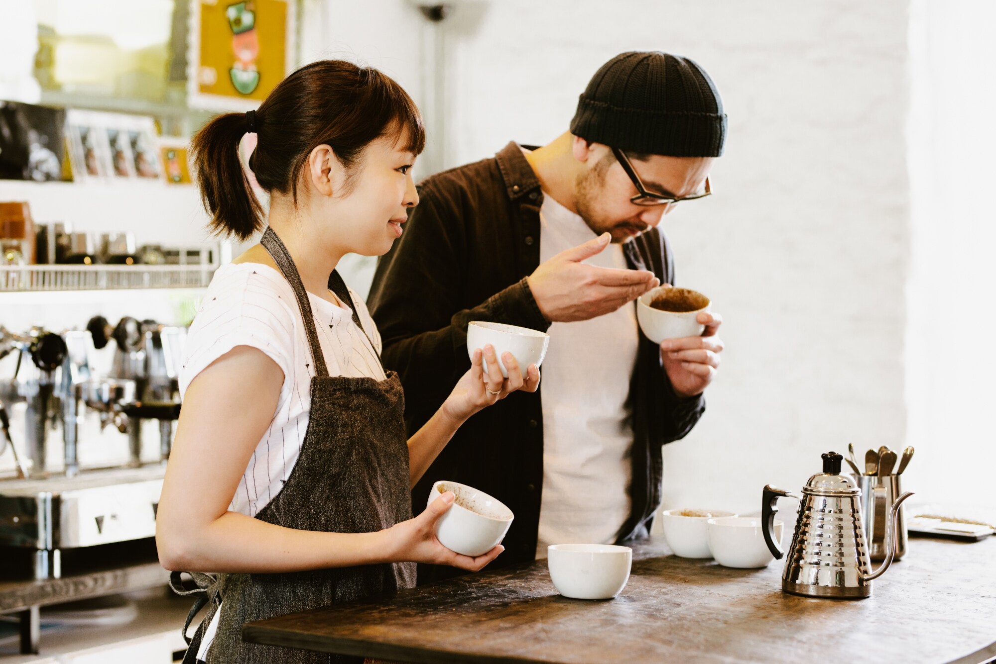 Zwei Menschen haben mehrere weiße Tassen mit Kaffee vor sich und riechen an ihnen