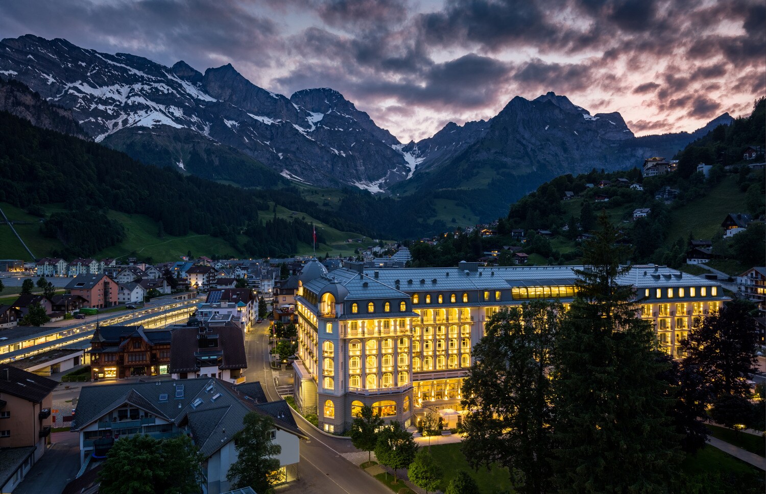 Ein hell erleuchtetes, schlossartiges Gebäude in einem Ort umgeben von Bergen Ein hell erleuchtetes, schlossartiges Gebäude in einem Ort umgeben von Bergen
