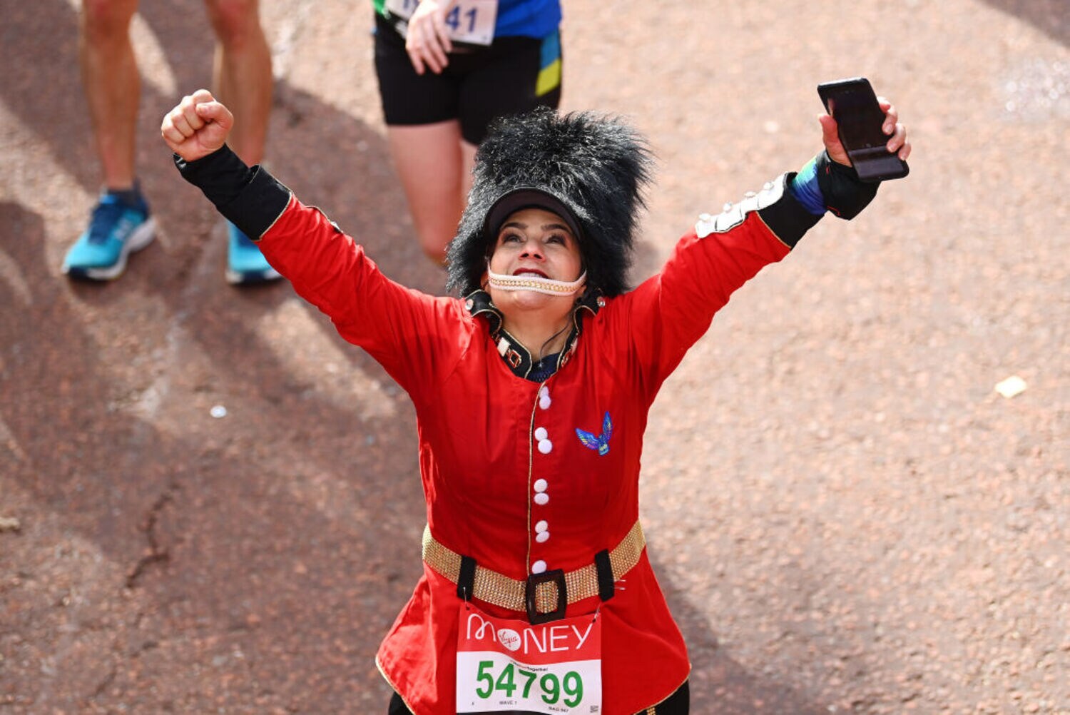 Eine Frau in roter Polizeitracht mit einer Teilnehmernummer des London Marathon reckt die Arme in die Höhe.