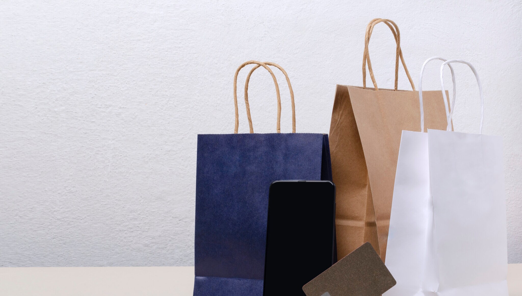 Einkaufstaschen, Kreditkarte und leerer Bildschirm des Smartphones vor einer weißen Wand