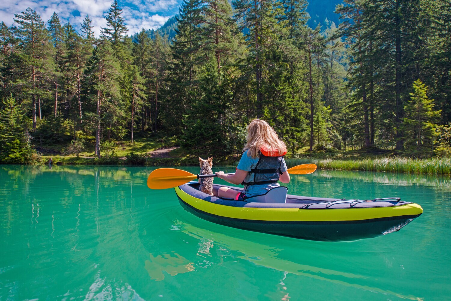 Eine Frau mit einem Hund im Kanu auf einem türkisfarbenen Fluss