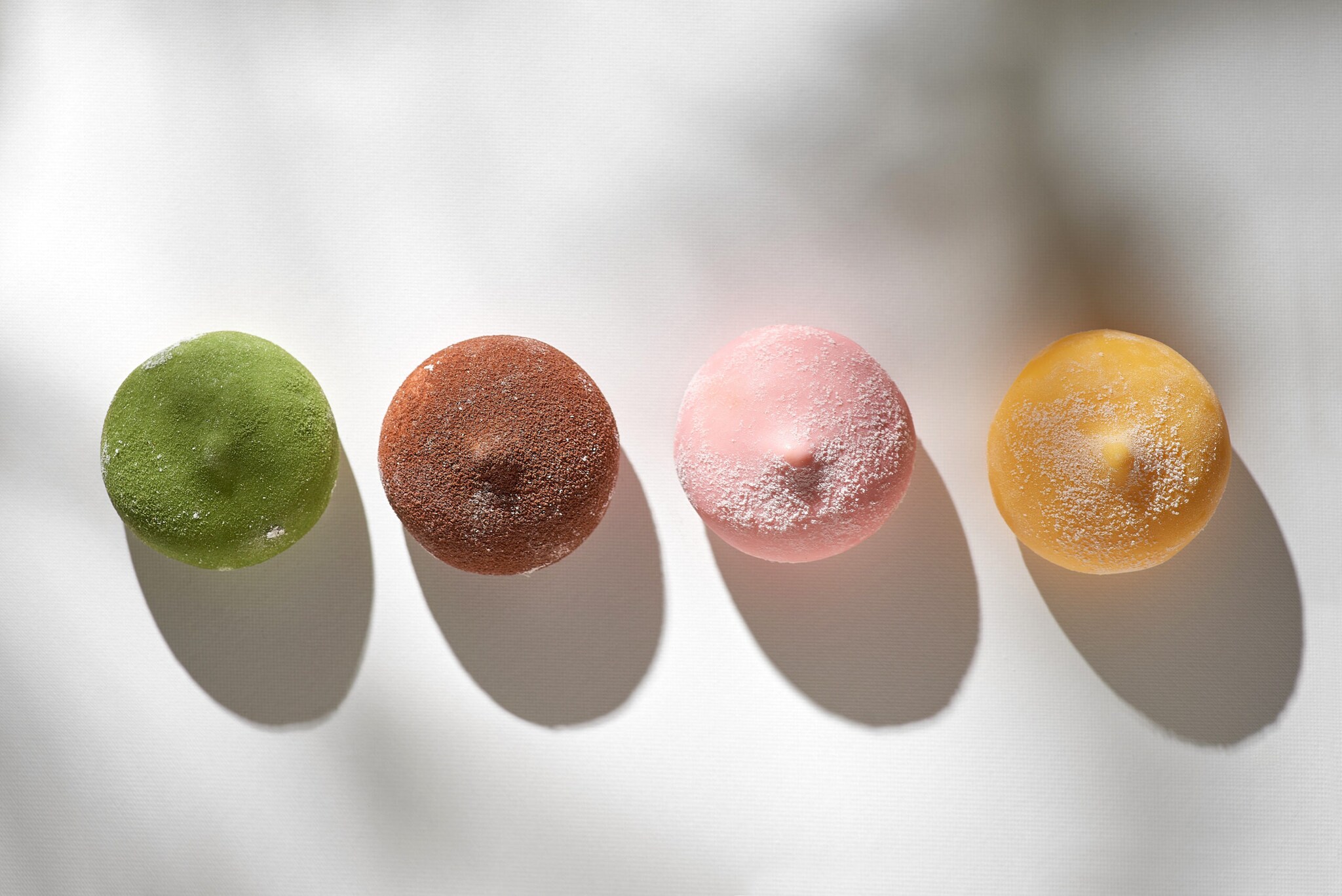 Auf einer hellen Unterlage liegen gefärbte und bestäubte Mochi-Eiskugeln.