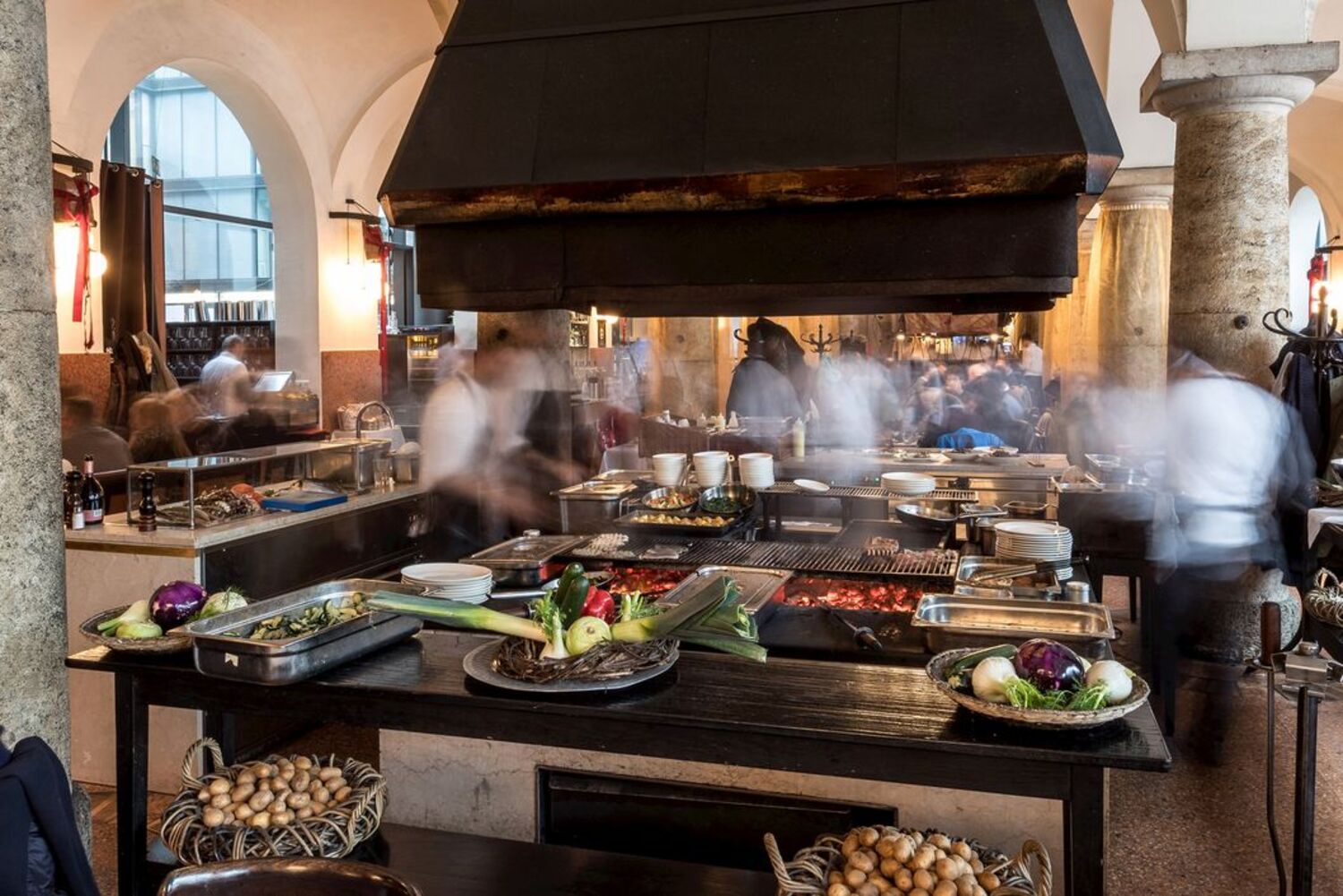 Unter einer großen Abzugshaube in einer Säulenhalle wird gekocht.