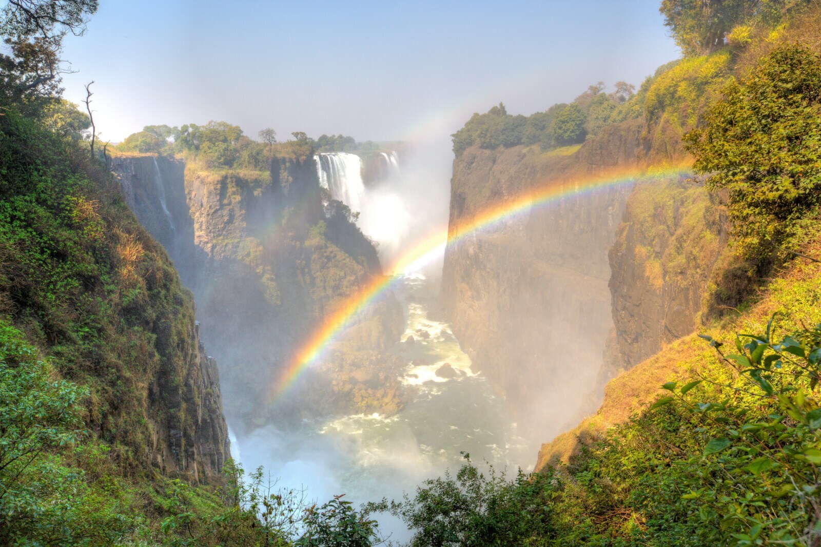 Panoramaansicht der Victoriafälle in Afrika, zwischen deren Felsen ein Regenbogen scheint