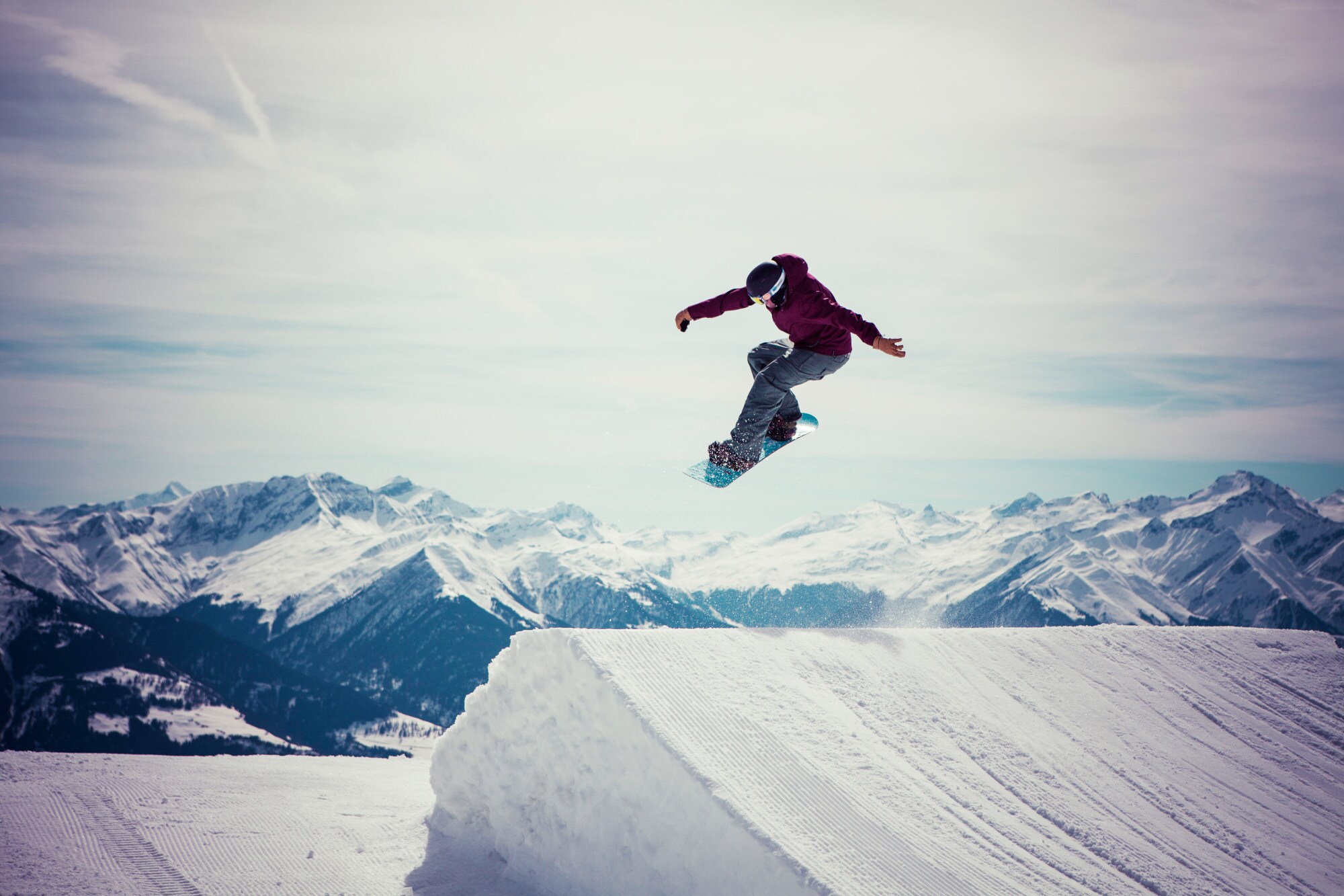 Ein Snowboarder springt über eine Schneeschanze vor Bergpanorama