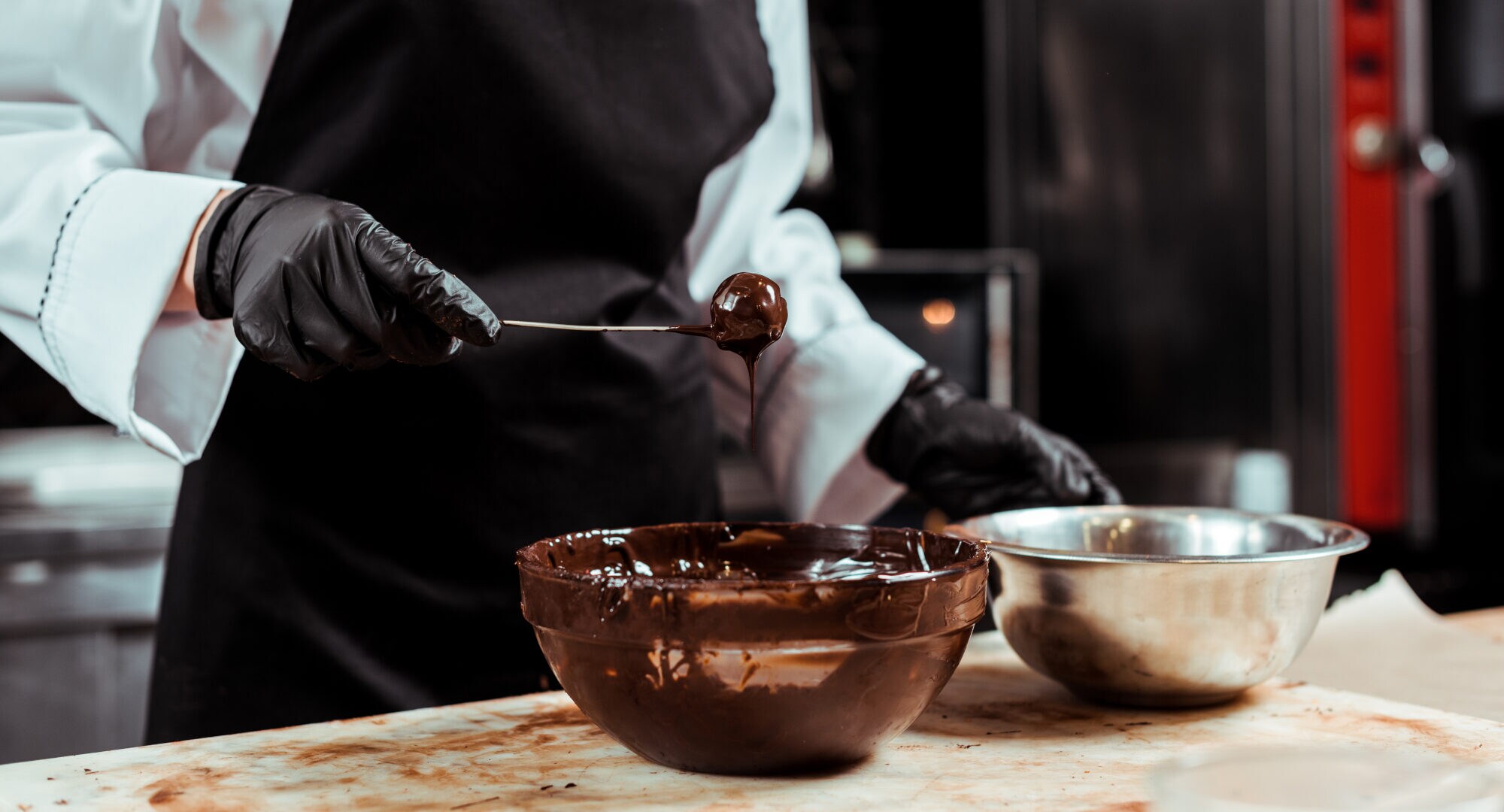 Ein Mensch mit Kochschürze hält einen schokoladigen Löffel über einer schokoladigen Schüssel Ein Mensch mit Kochschürze hält einen schokoladigen Löffel über einer schokoladigen Schüssel
