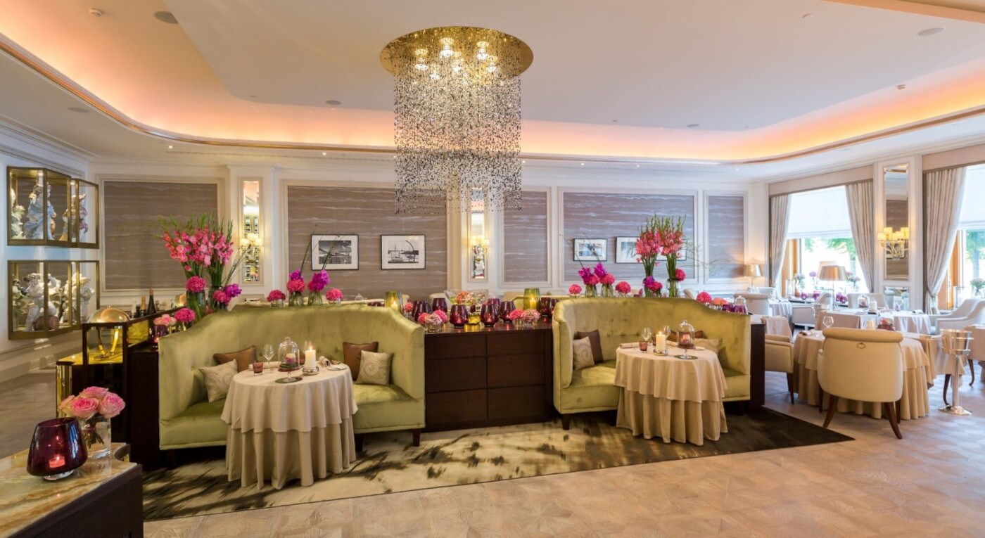 Ein großer Raum mit samtbezogenen Sitzecken, Tischen und rosa Blumen