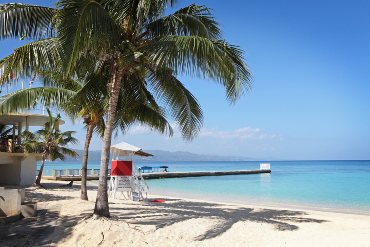 Ein Strand mit Palmen, einem Aufsichtsturm und einem langen Steg ins Wasser