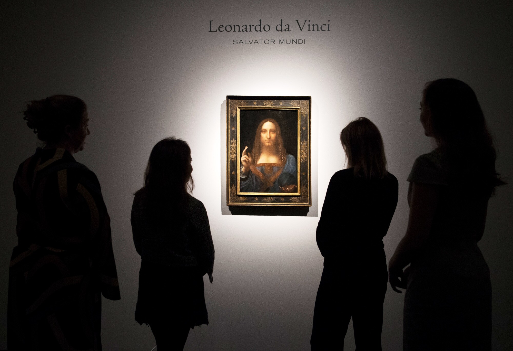Rückansicht mehrerer Personen als Silhouetten, die Leonardo da Vincis Gemälde Salvator Mundi in einem goldenen Rahmen an einer weißen Wand betrachten