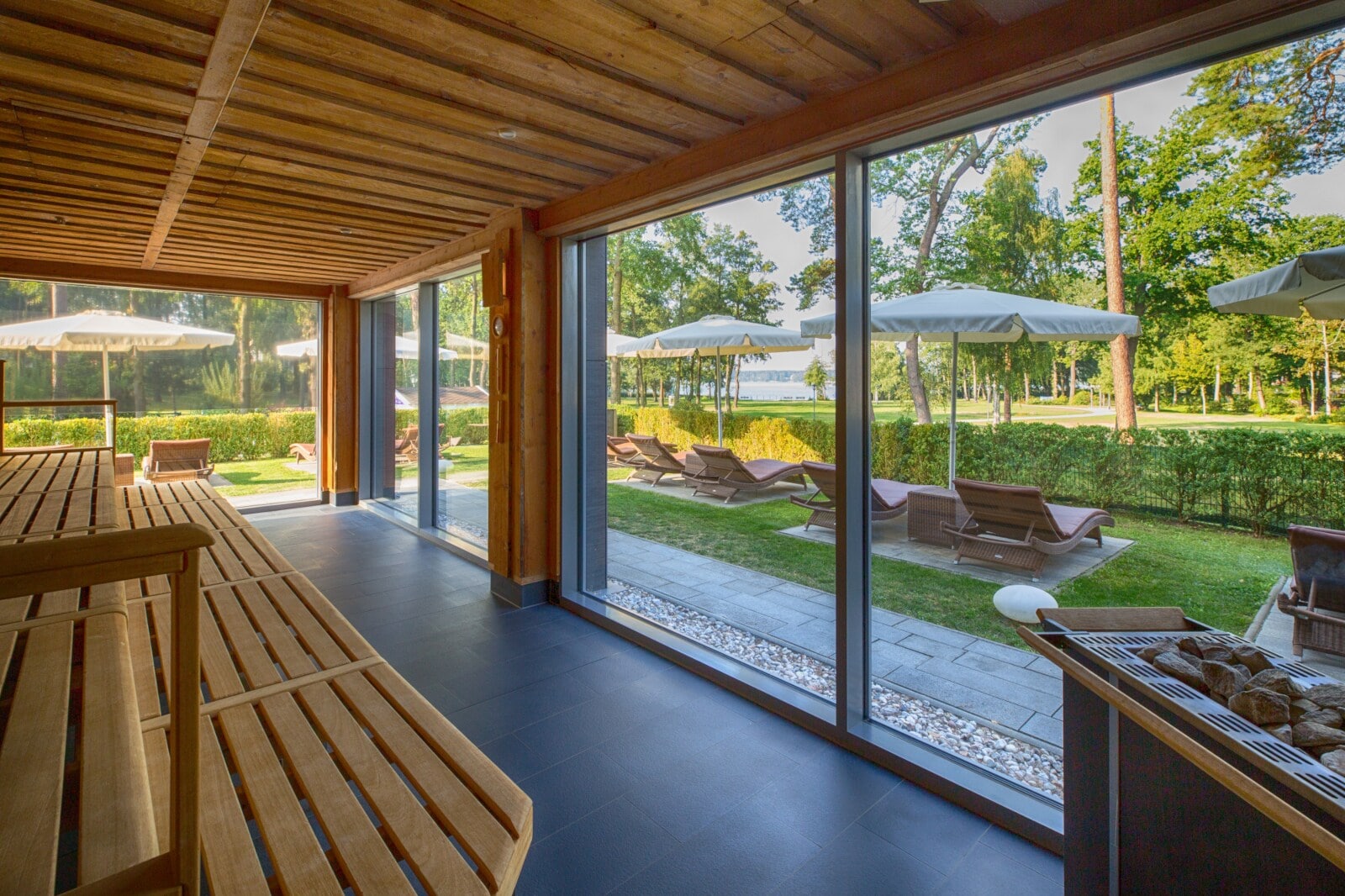 Eine Holzsauna mit Blick in einen Garten mit Liegen an einem See Eine Holzsauna mit Blick in einen Garten mit Liegen an einem See