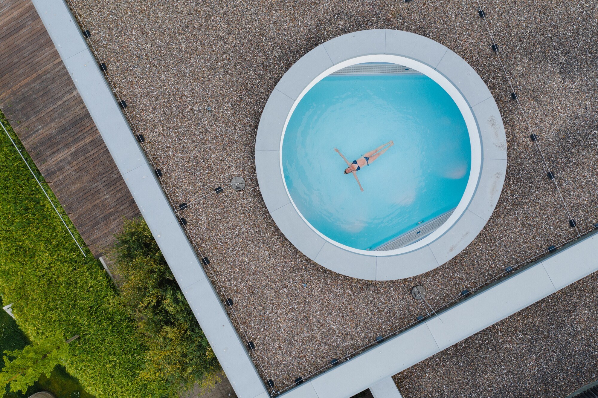 Eine Frau schwebt mit ausgestreckten Armen in einem Pool, fotografiert durch ein rundes Dachfenster aus der Vogelperspektive