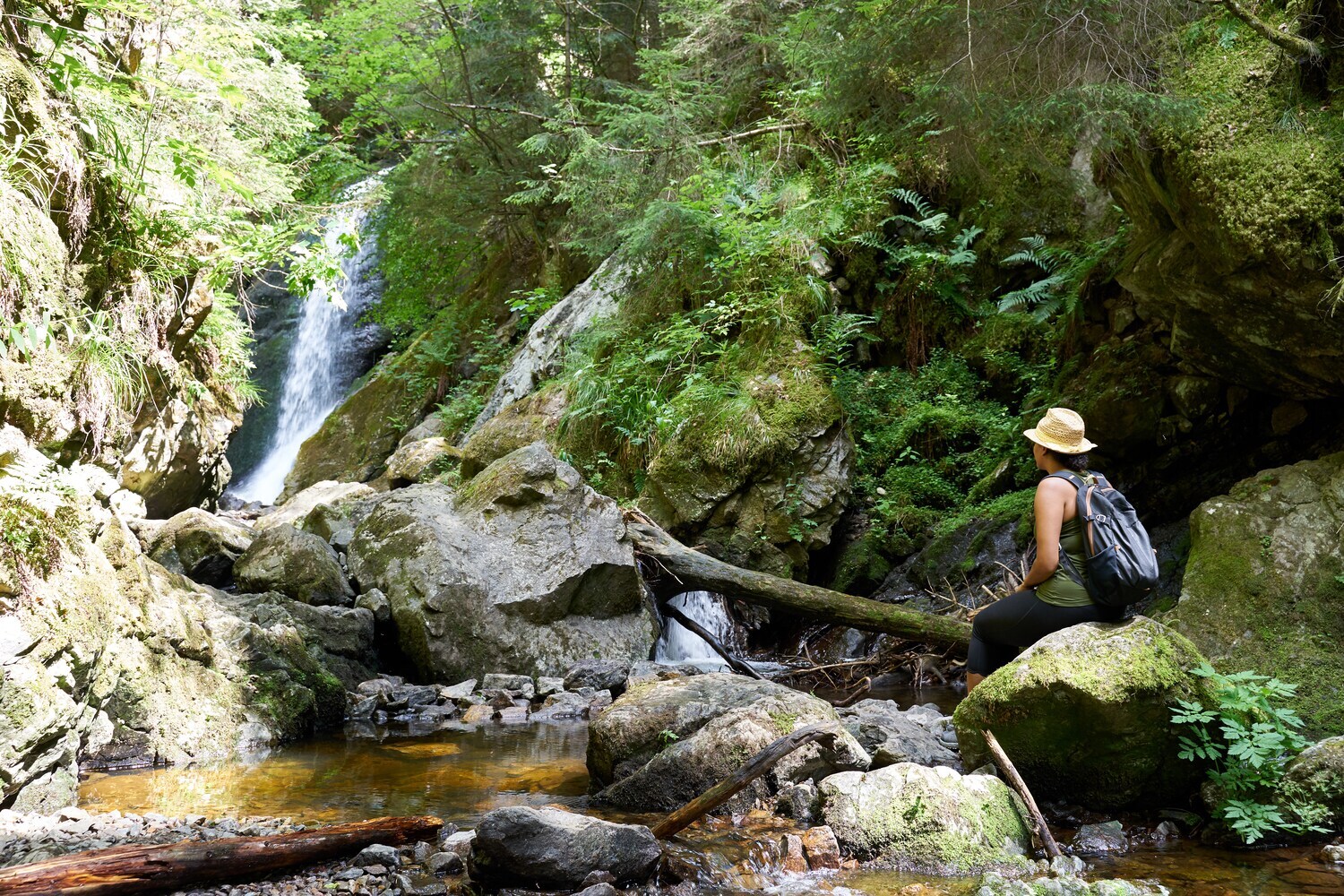 Eine Frau sitzt auf einem Felsen vor einem Wasserfall Eine Frau sitzt auf einem Felsen vor einem Wasserfall