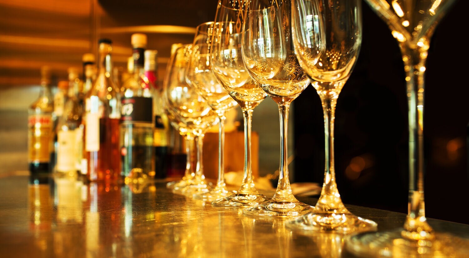 Eine Reihe Weingläser und Flaschen alkoholischer Getränke dahinter