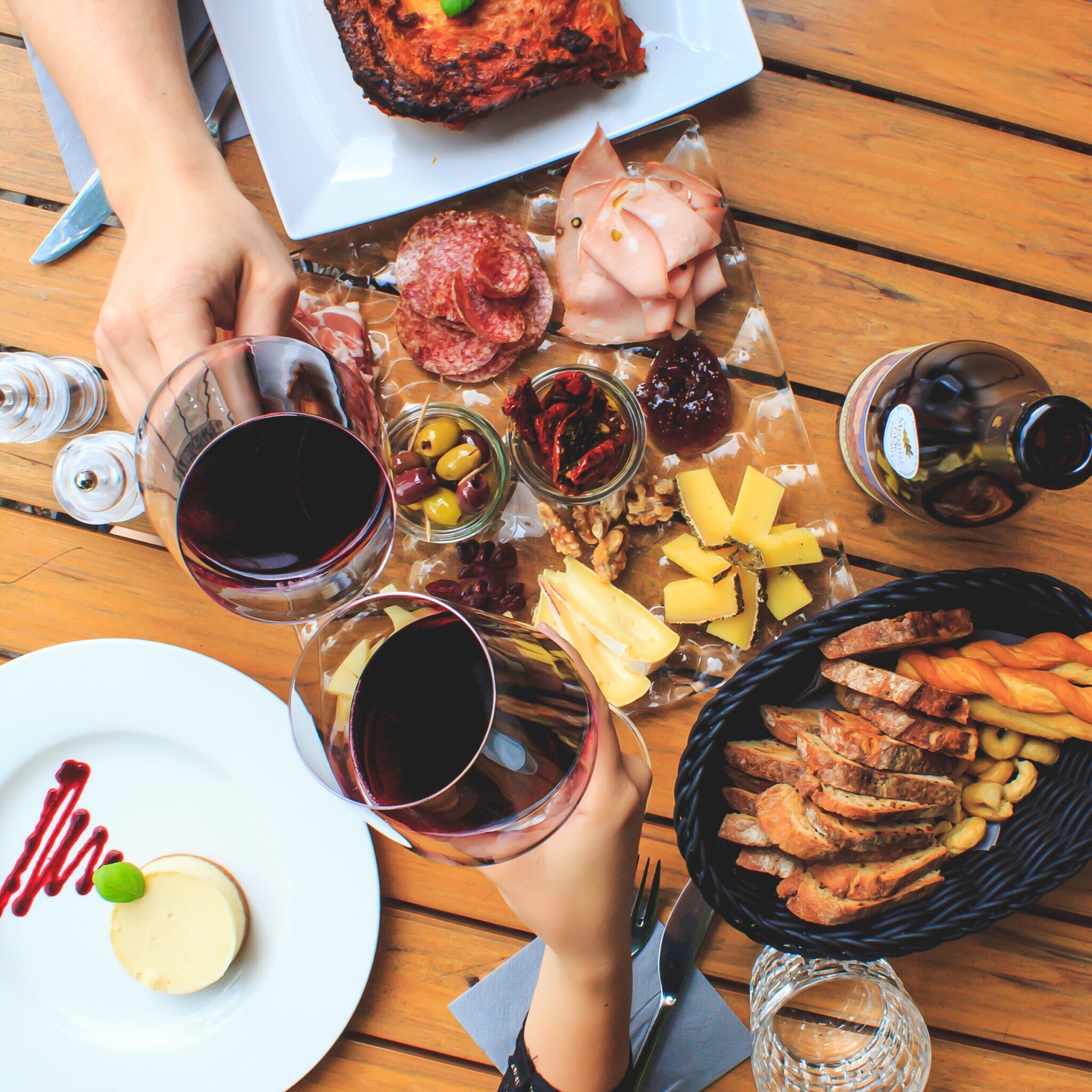 Zwei Personen stoßen mit Rotwein an, auf dem Tisch sind verschiedene Snacks verteilt