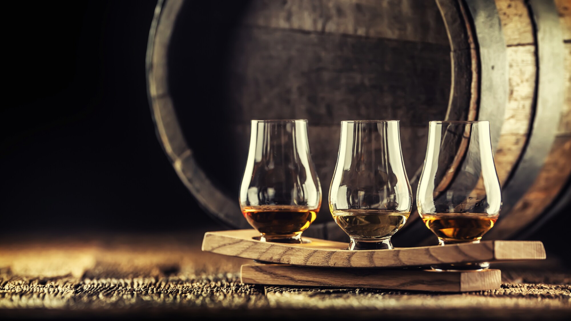 Drei Glencairn-Glöser mit Whisky auf einem Servierbrett vor einem Whiskyfass