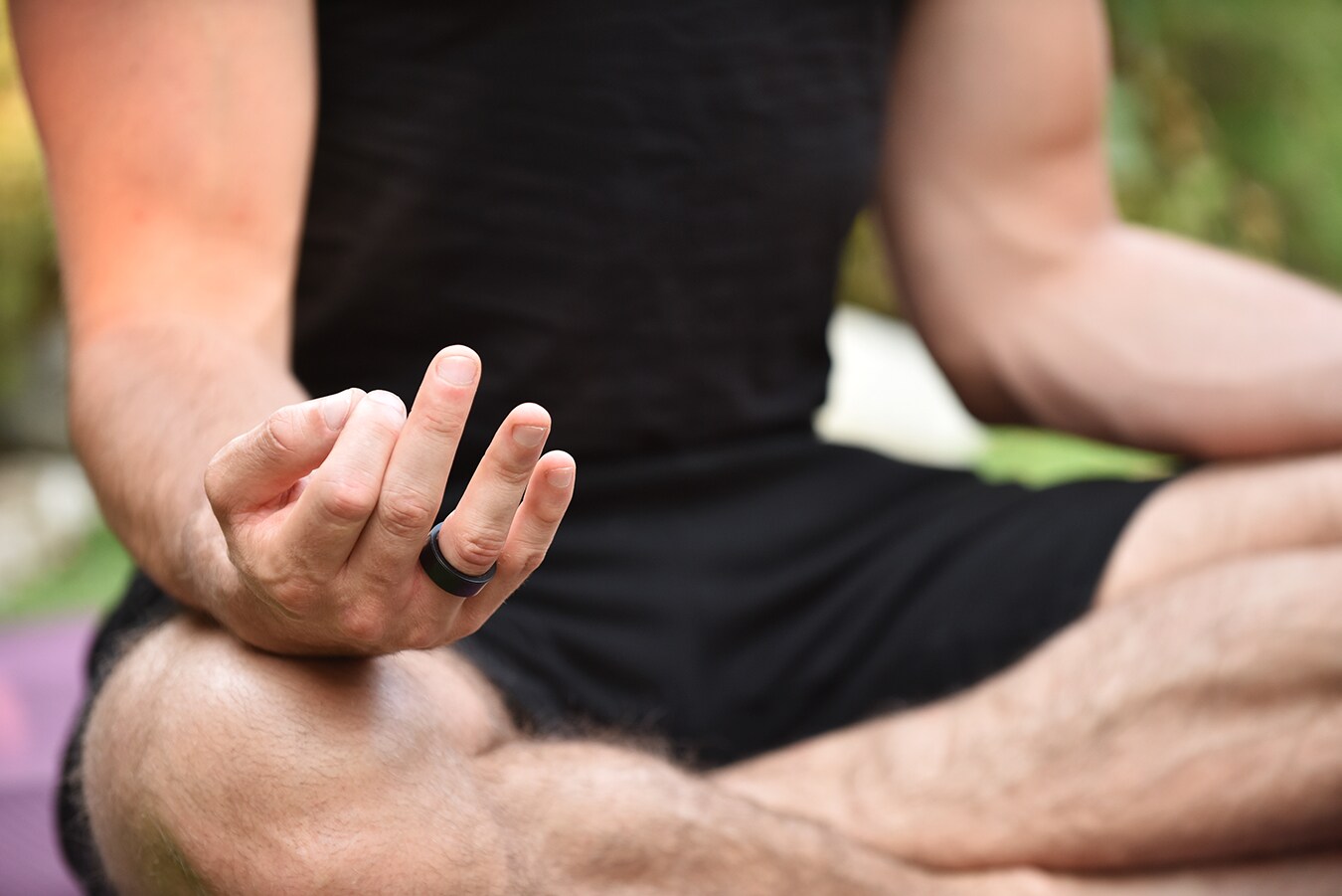 Ein Mann im Schneidersitz mit einem schwarzen Ring am Finger