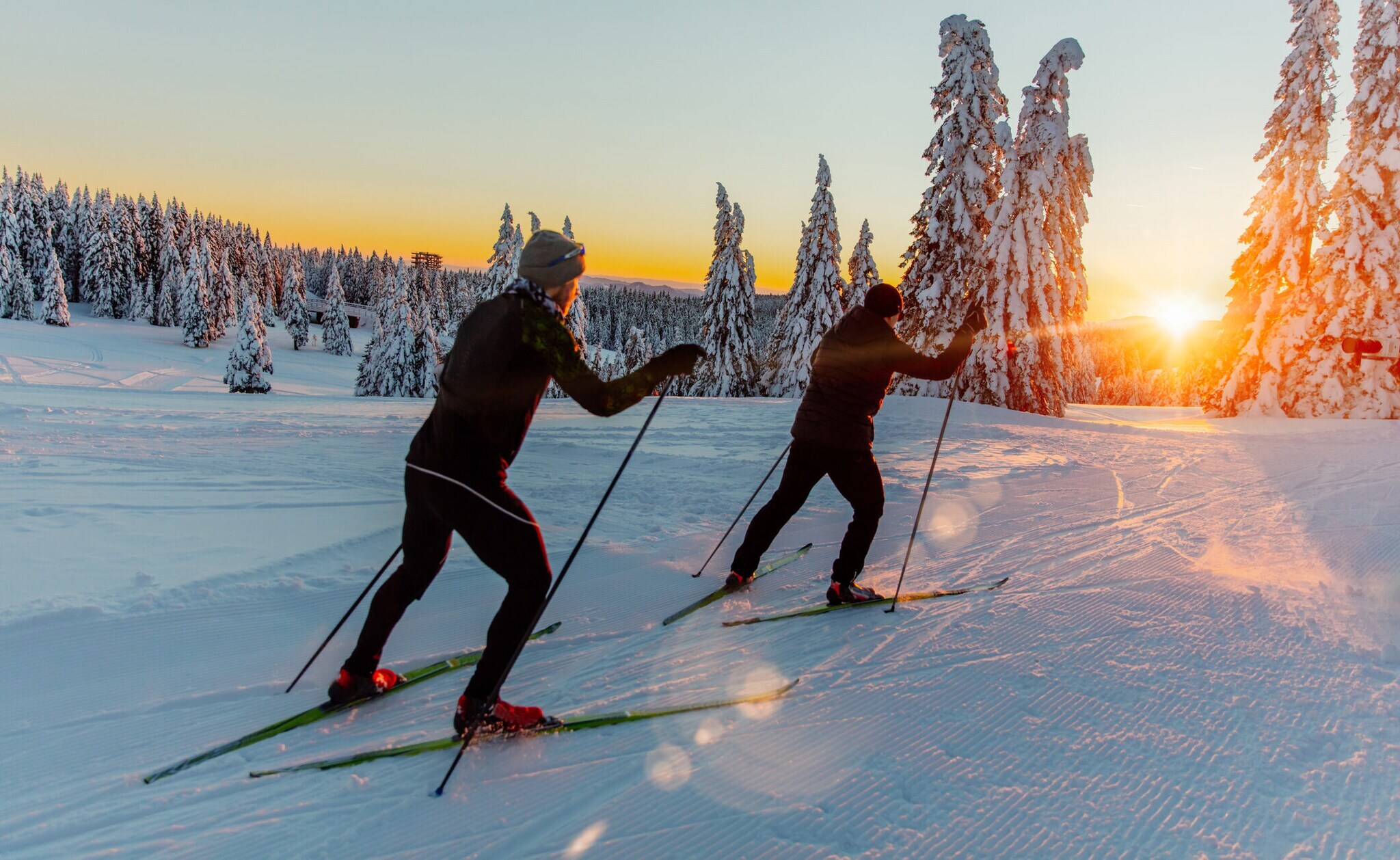 Zwei Männer auf Skiern fahren dem Sonnenuntergang entgegen.