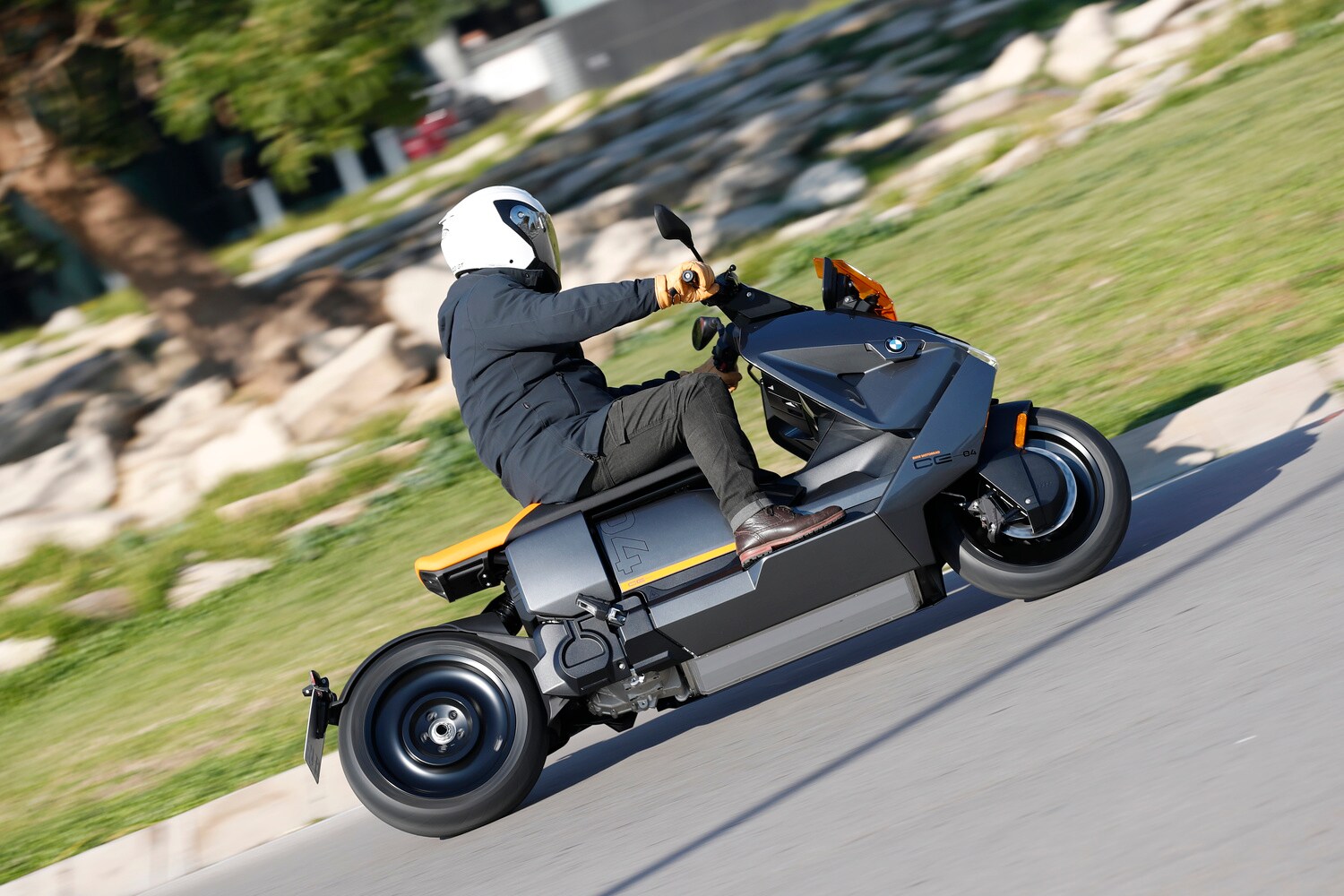 Ein grauer BMW CE 04 mit orangefarbenem Windschild fährt in einem Kreisverkehr. Ein grauer BMW CE 04 mit orangefarbenem Windschild fährt in einem Kreisverkehr.