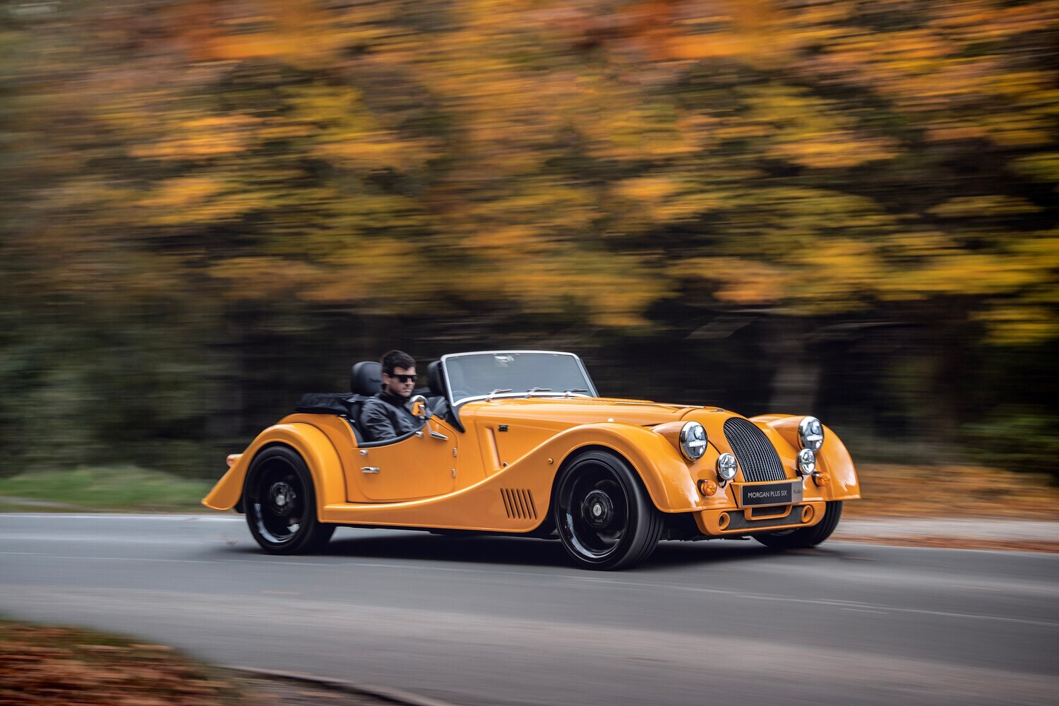 Ein gelber Roadster fährt auf einer Straße entlang.