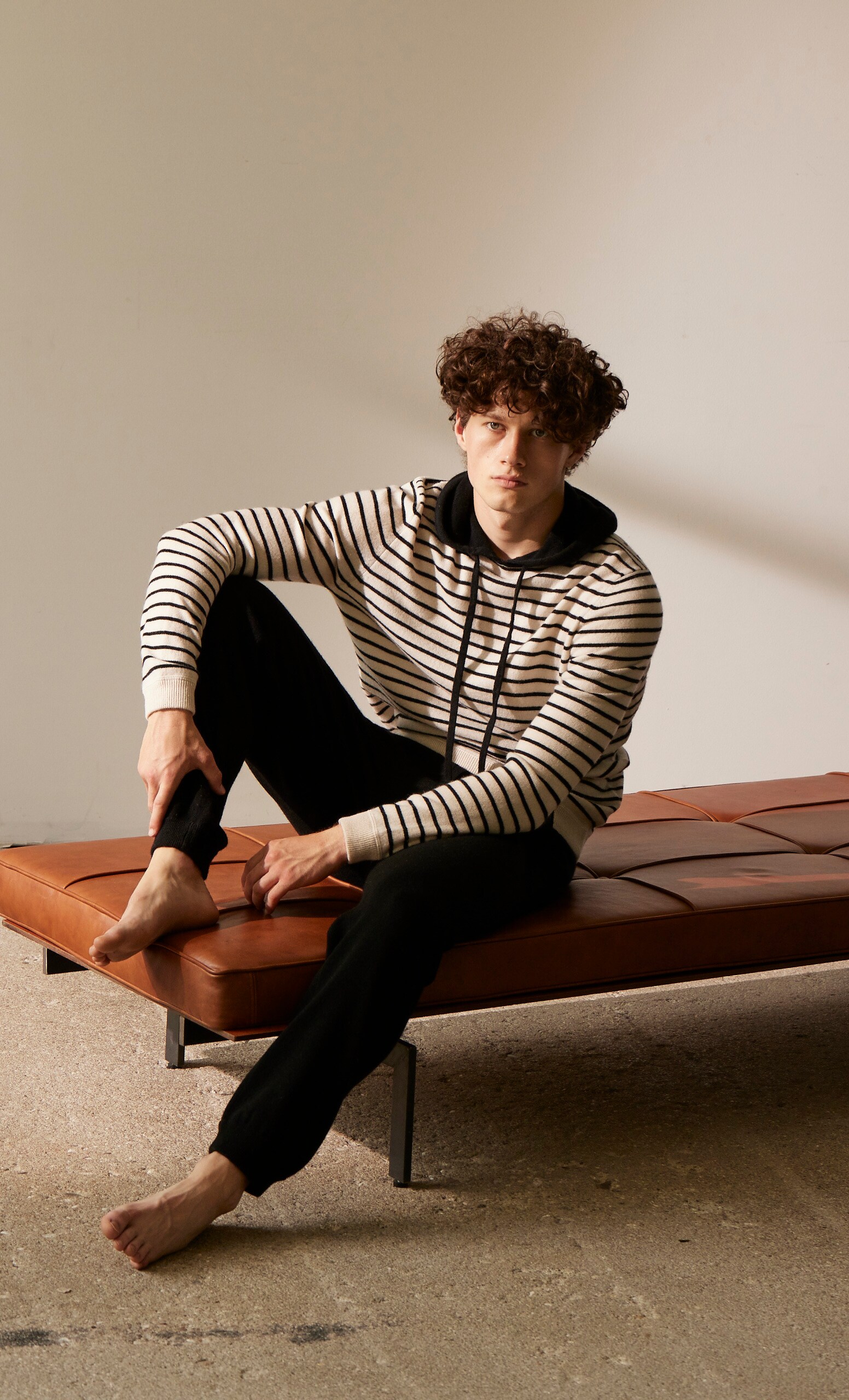 Ein Mann mit geringeltem Wollpullover sitzt auf einer Lederbank Ein Mann mit geringeltem Wollpullover sitzt auf einer Lederbank