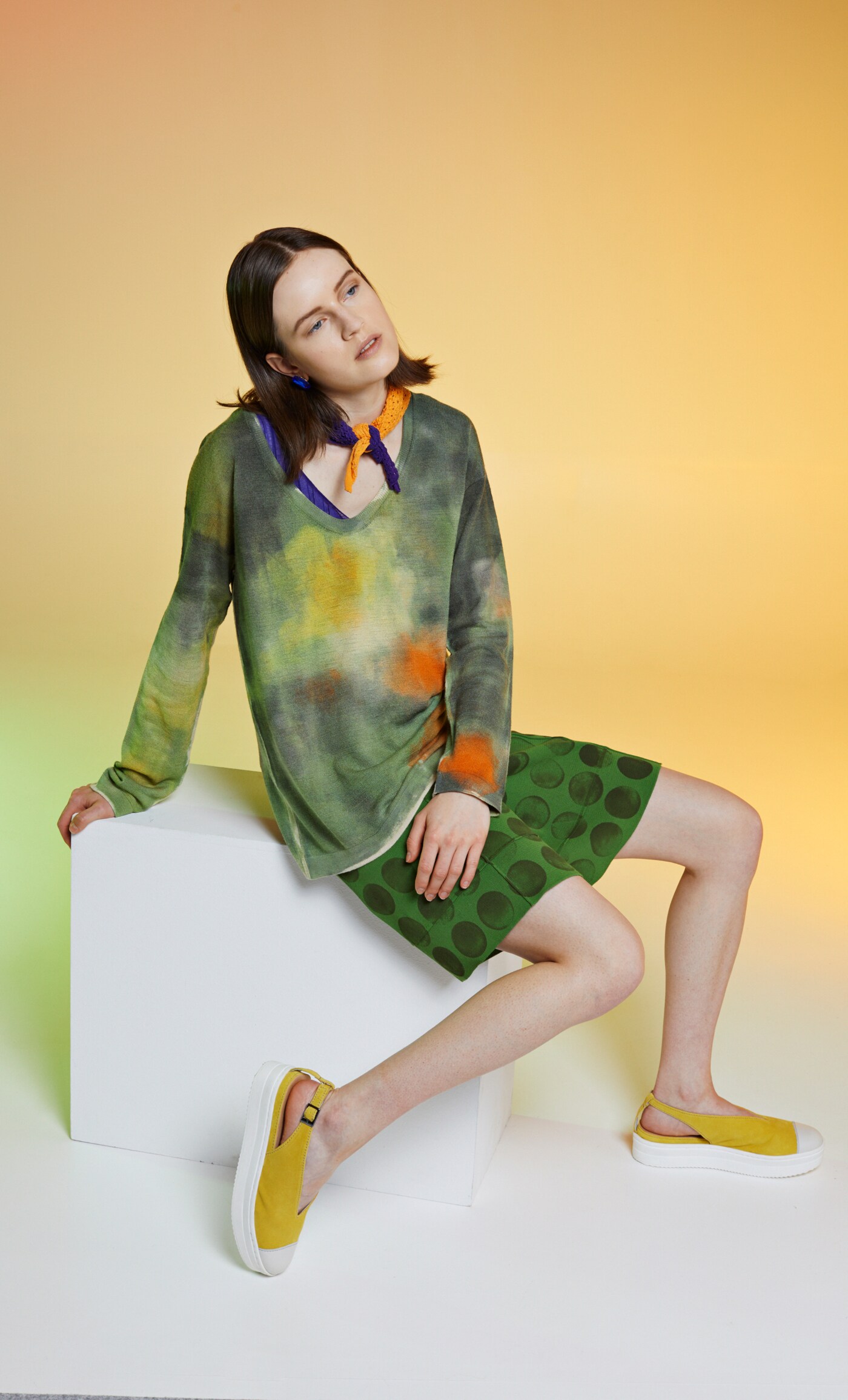 Eine Frau im farbenfrohen Outfit sitzt auf einem Kubus Eine Frau im farbenfrohen Outfit sitzt auf einem Kubus