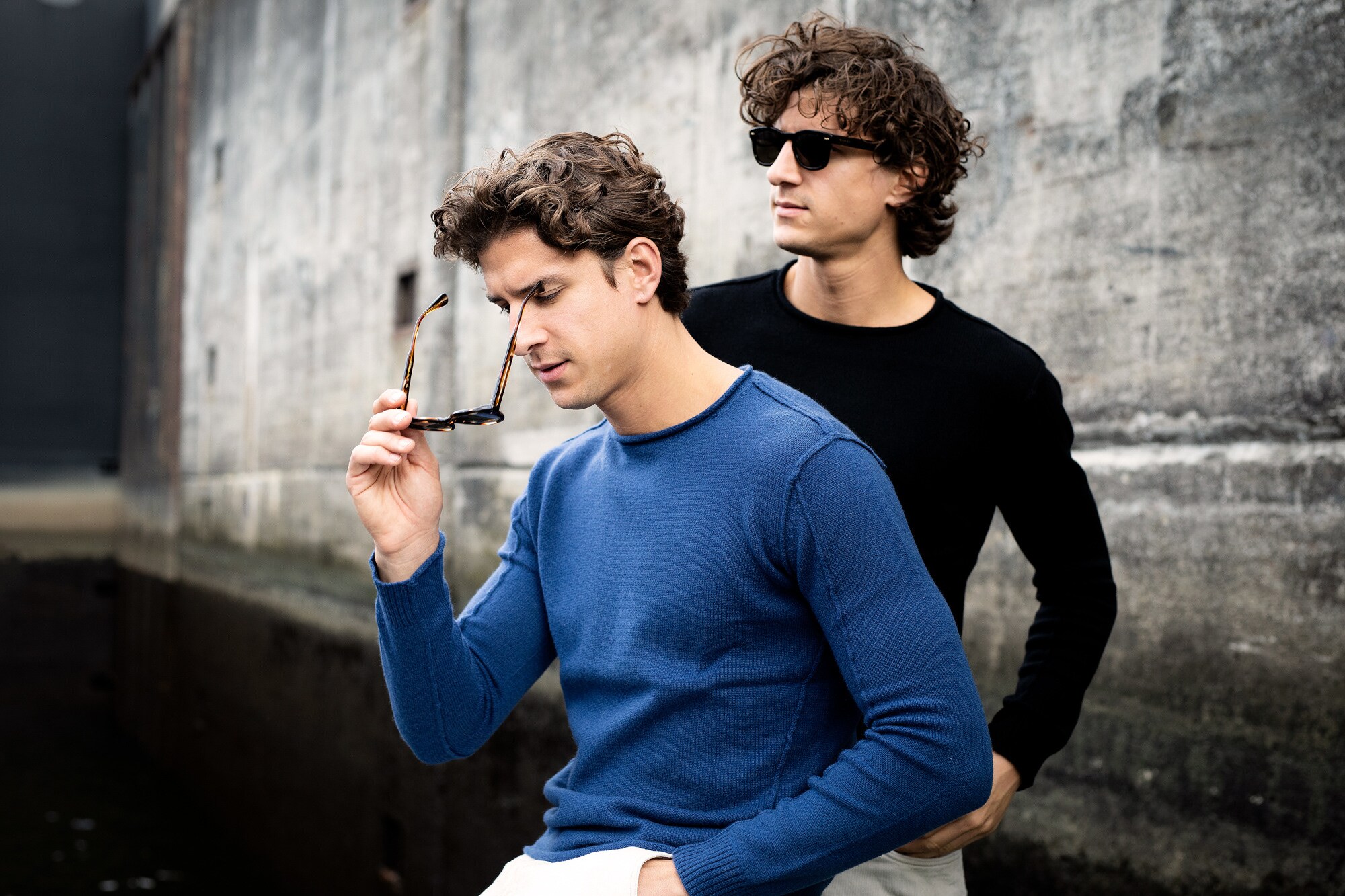 Zwei Männer mit Wollpullovern stehen vor einer Betonwand