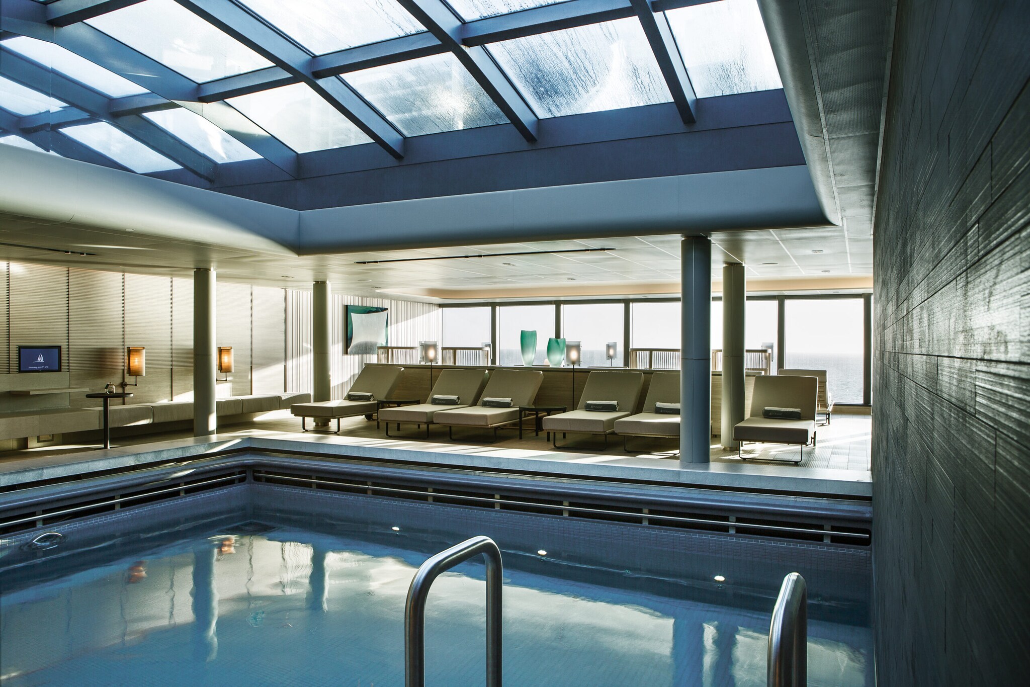 Pool mit Liegen in einem Raum mit großen Fenstern