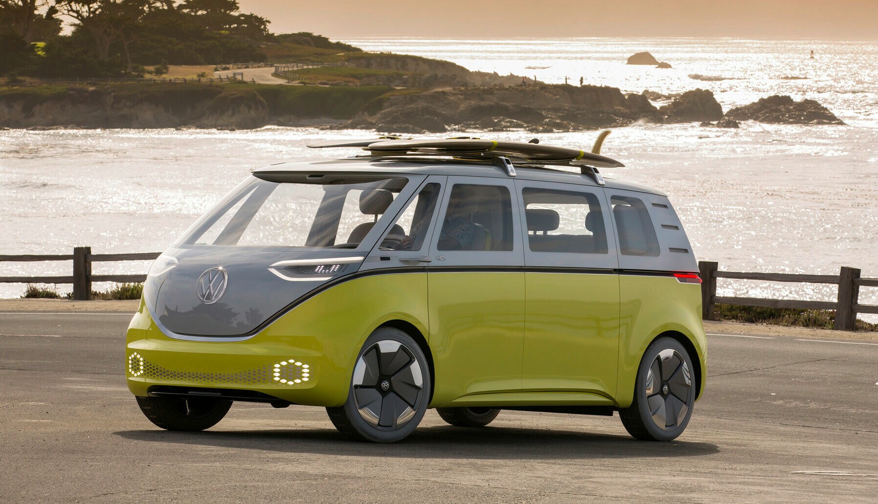 Ein Elektrobulli ID. Buzz am Meer mit zwei Surfbrettern auf dem Dach