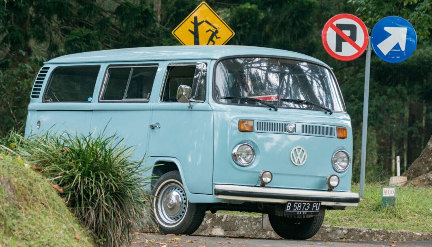 Ein hellblauer VW Bus T2 auf einer Straße mit bunten Straßenschildern Ein hellblauer VW Bus T2 auf einer Straße mit bunten Straßenschildern