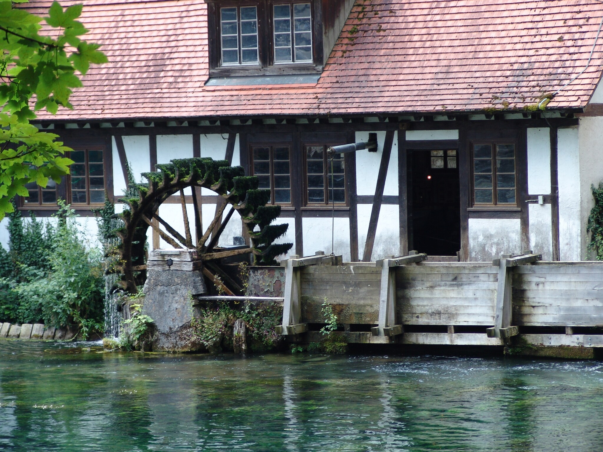 Eine Mühle mit Wassermühle vor einem Gewässer.