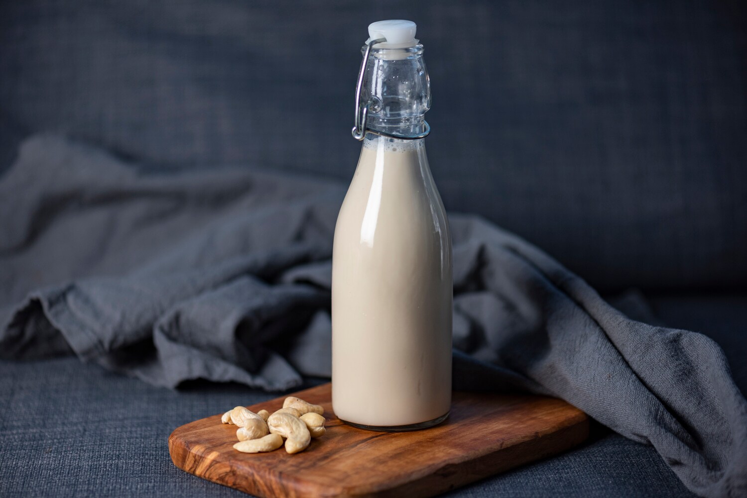 Neben einer Flasche mit Cashewmilch liegen einige Cashewnüsse.