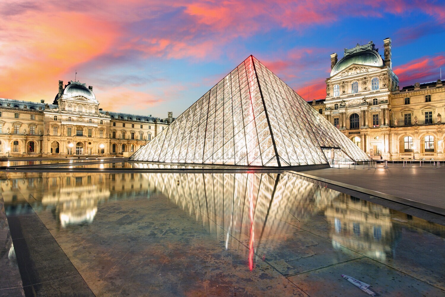 Das dreieckige verglaste Gebäude des Louvre ist hell beleuchtet.