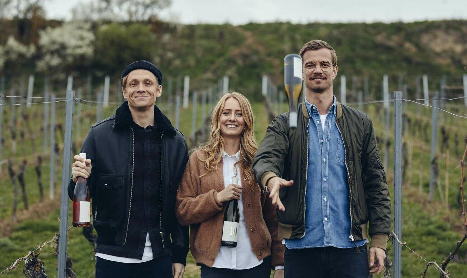 Matthias Schweighöfer, Juliane Eller und Joko Winterscheidt mit Weinflasche vor einem Weinberg