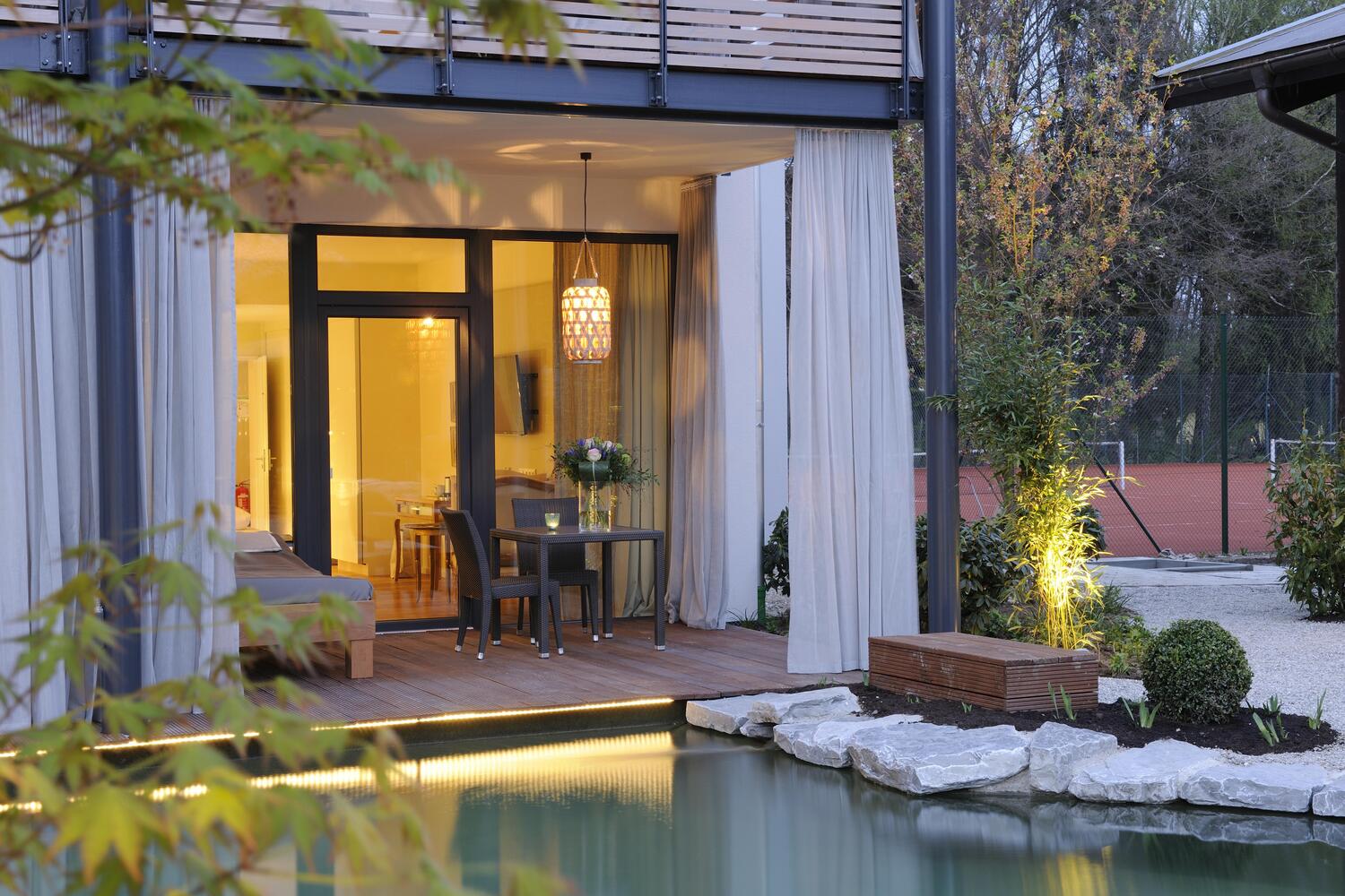 Die Terrasse eines Hotelzimmers, davor ein Naturteich, im Hintergrund ein Tennisplatz Die Terrasse eines Hotelzimmers, davor ein Naturteich, im Hintergrund ein Tennisplatz